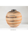 Close-up of a round ceramic artisan vase with swirled earth-tone design on a white surface against a plain background.