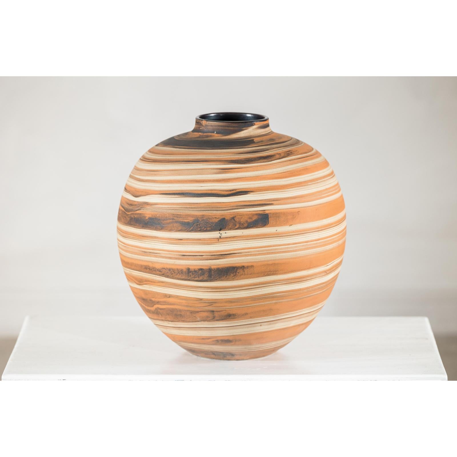 Close-up of round ceramic vase with swirled earth-tone design on white surface, plain background.