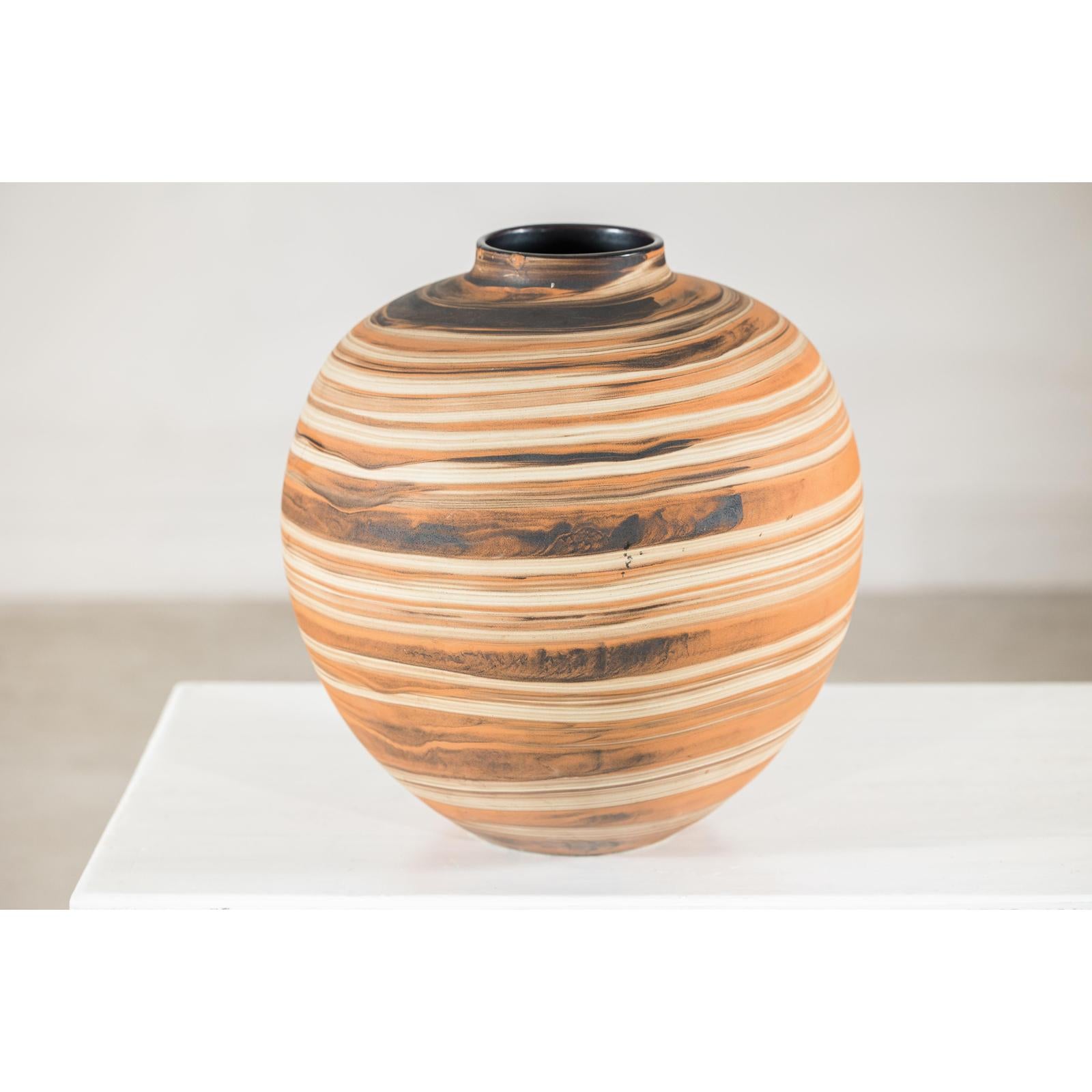 Earth-tone ceramic vase with swirled pattern, round shape, close-up on white surface.
