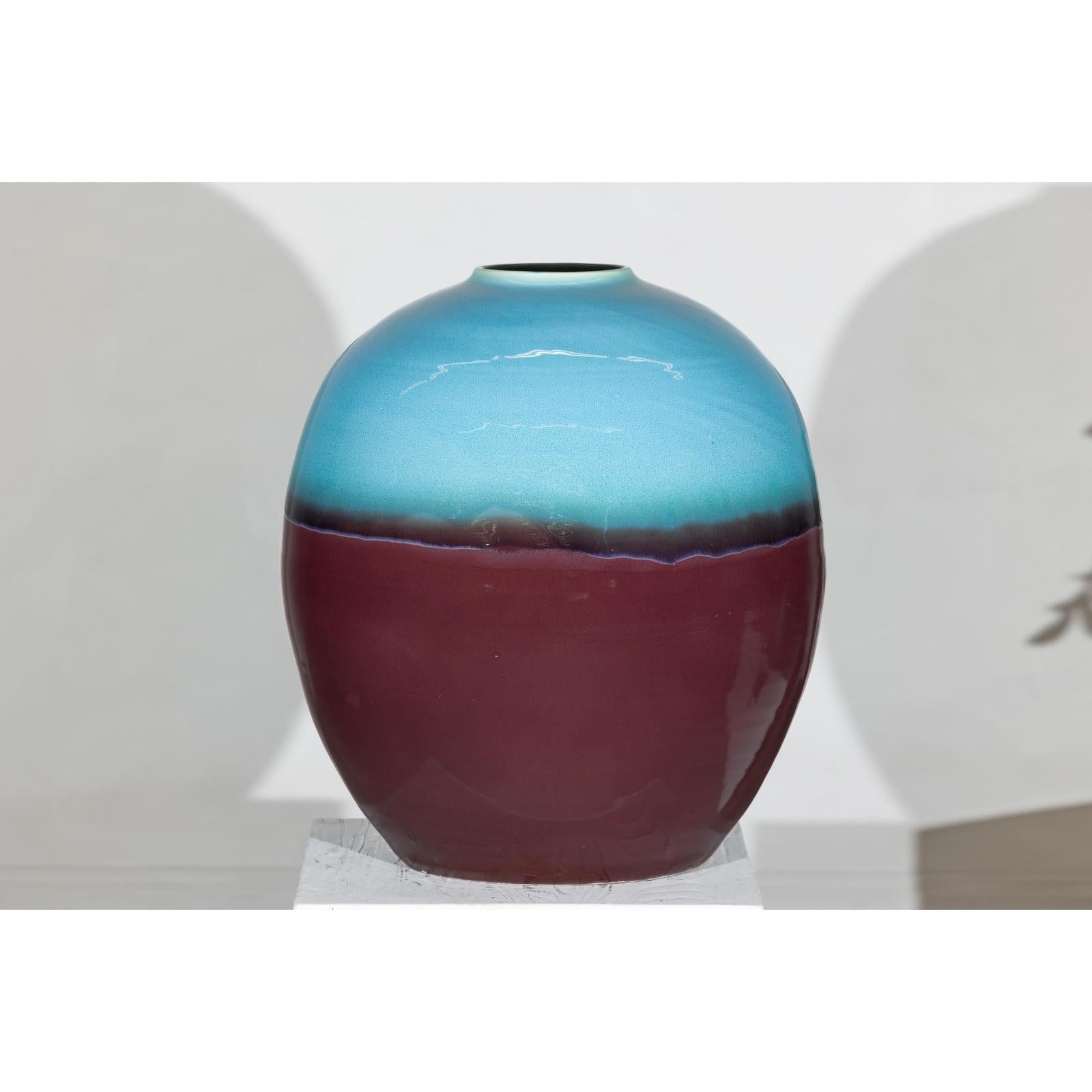 Turquoise and brown ceramic vase, round shape, close-up on white pedestal.