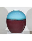 Turquoise and brown ceramic vase, round shape, close-up on white pedestal.
