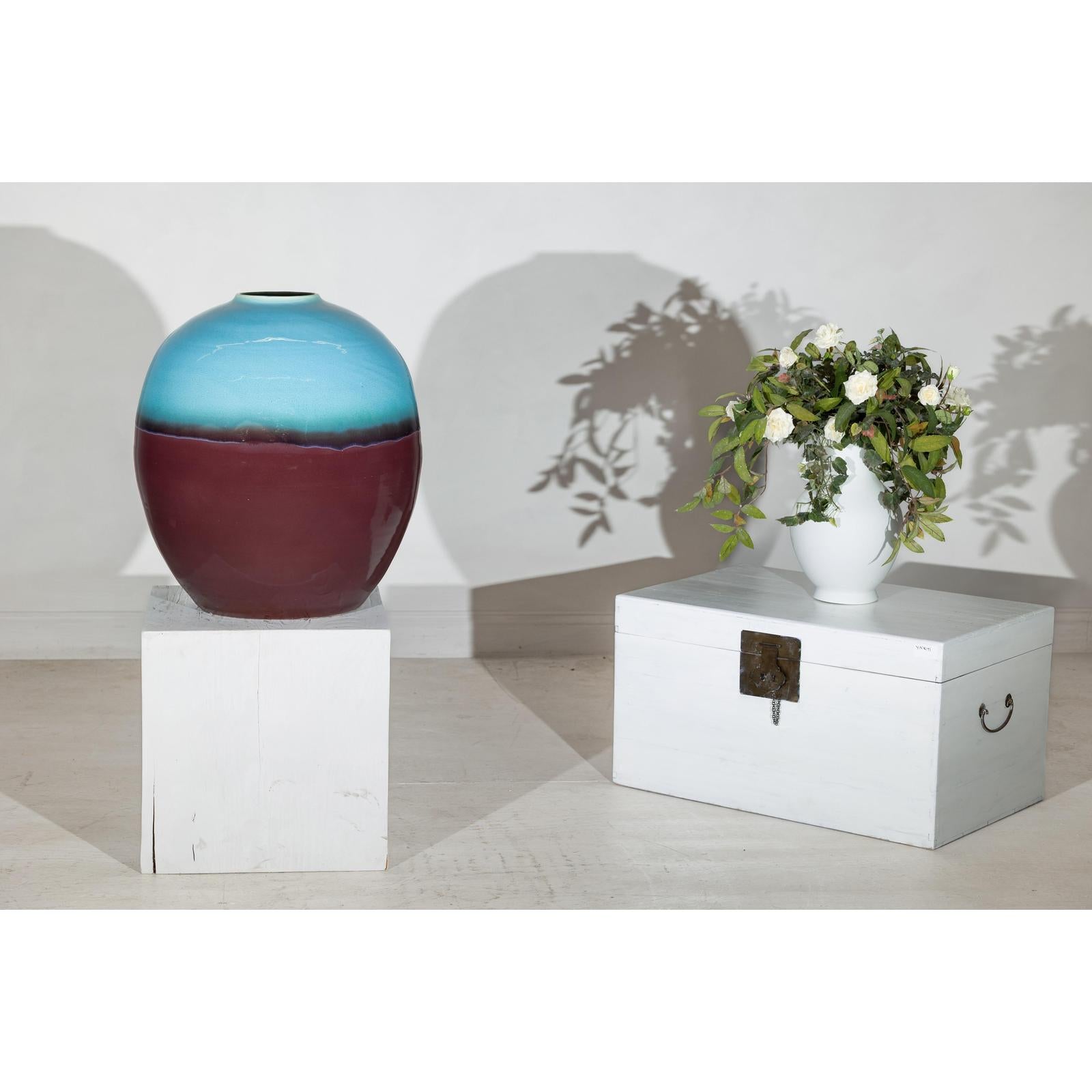 Turquoise and brown round ceramic vase next to white chest and floral white vase on display.