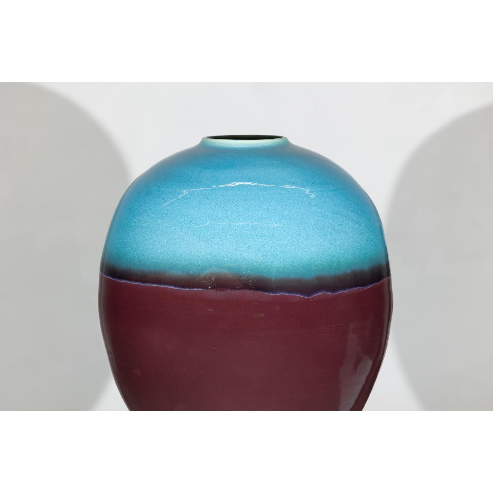 Close-up of round ceramic vase with turquoise glaze fading into brown, displayed on a plain white background.