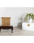 Square rattan storage box with side handles on a wooden table next to a white chest and flowers, country style.