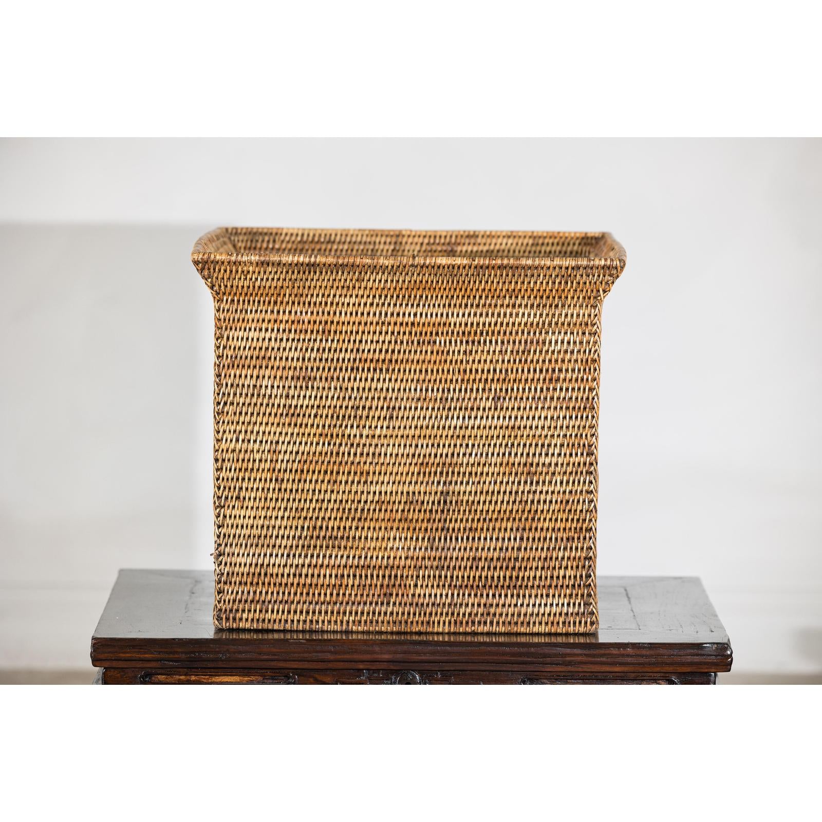 Square vintage rattan storage box with side handles on dark wood table, white background.