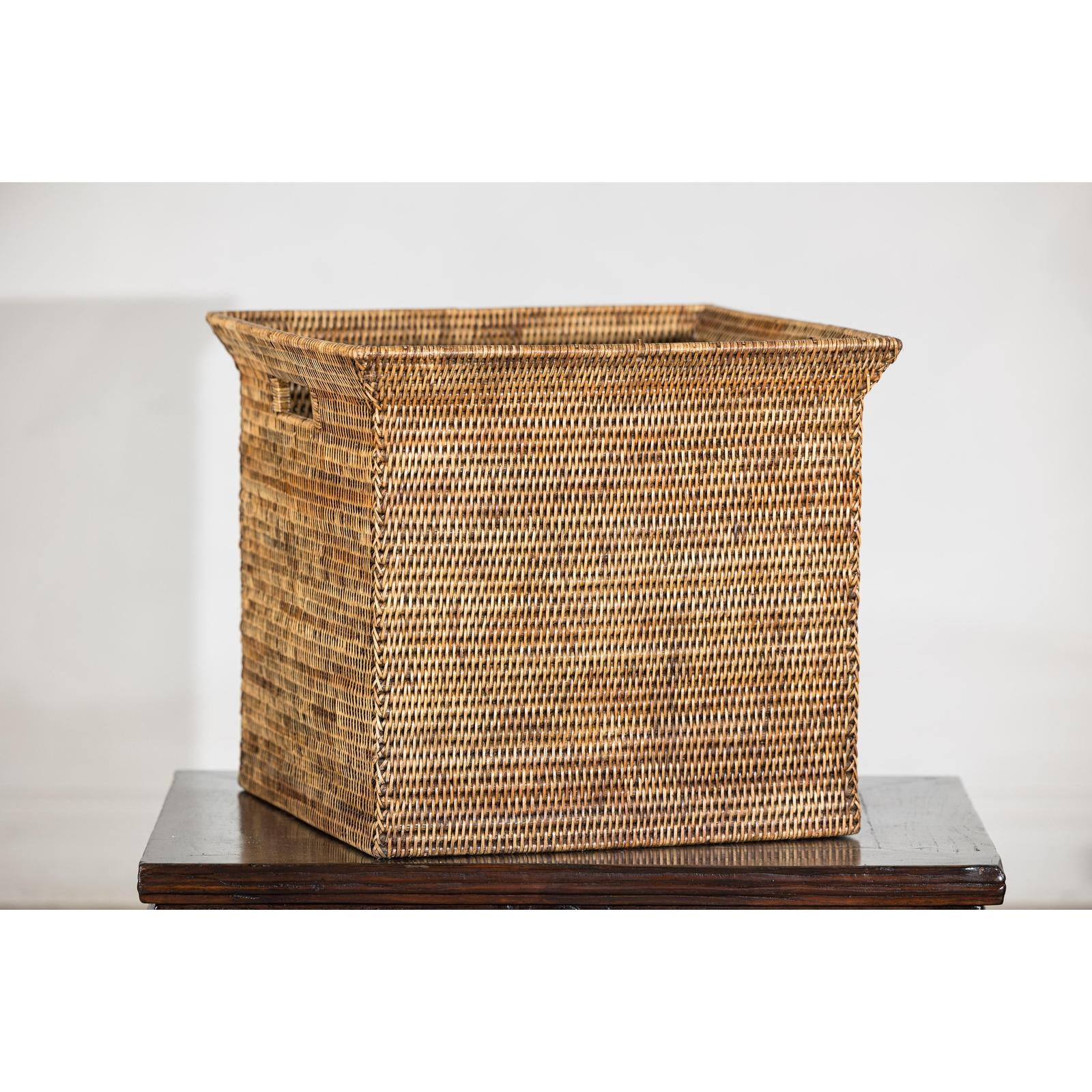 Square vintage rattan storage box with side handles on dark wood table, plain background, country style.