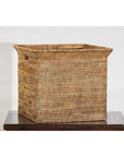 Square vintage rattan storage box with side handles on dark wood table, plain background, country style.