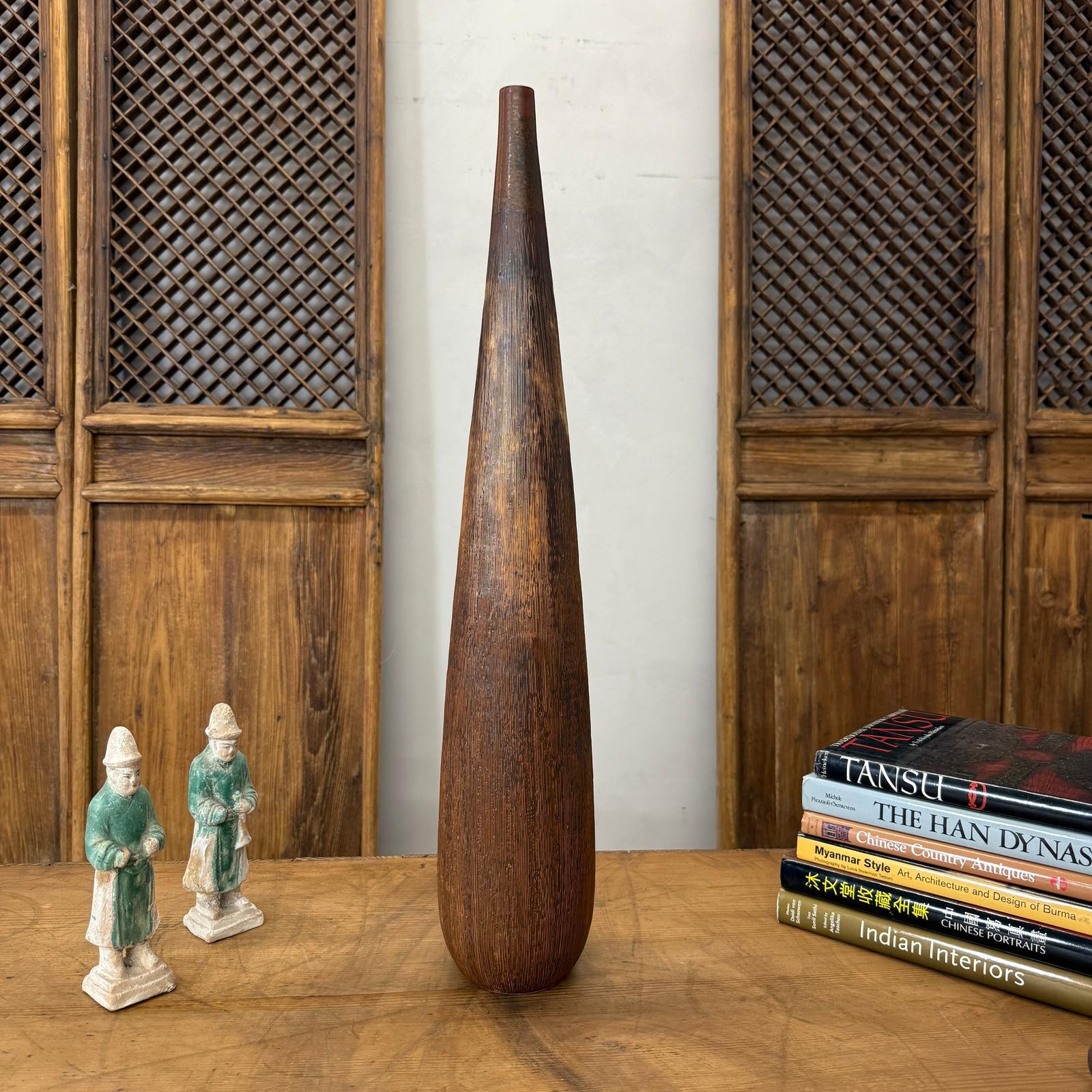 Brown and copper textured ceramic vase on a table with two figurines and books.