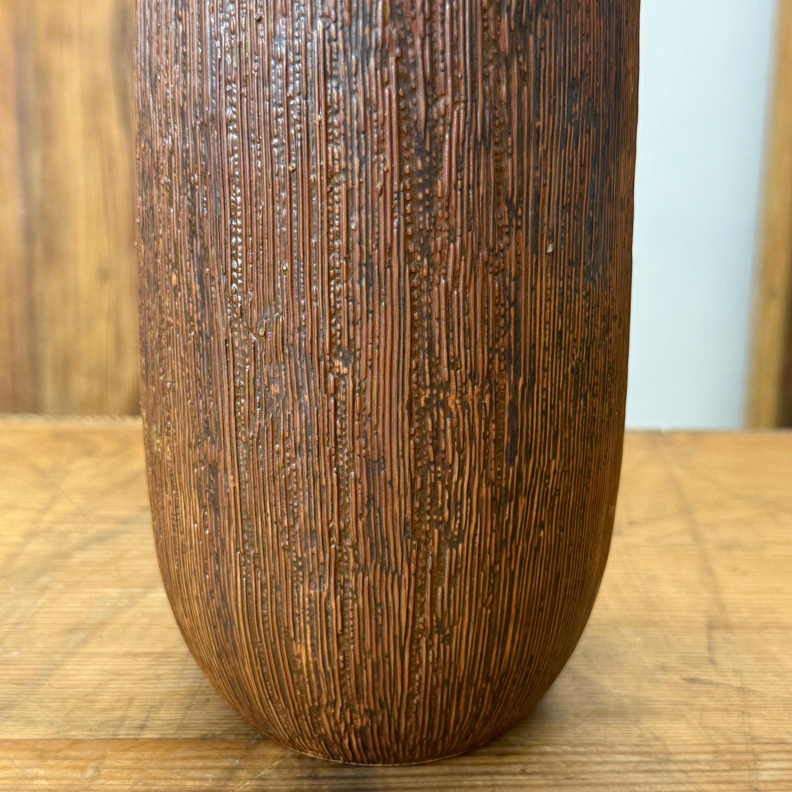 Close-up of brown and copper ceramic vase with vertical grooves on wooden surface.