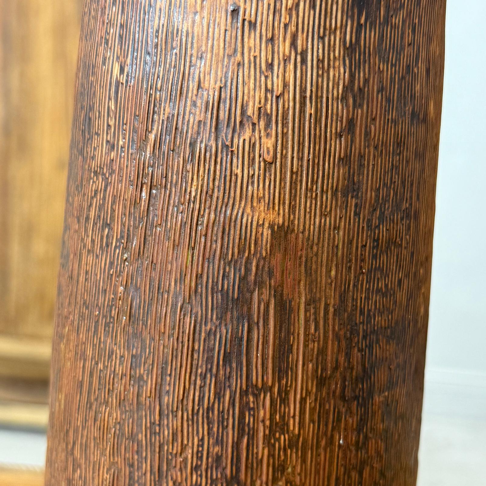 Close-up of a textured brown and copper ceramic vase against a textured brown background.