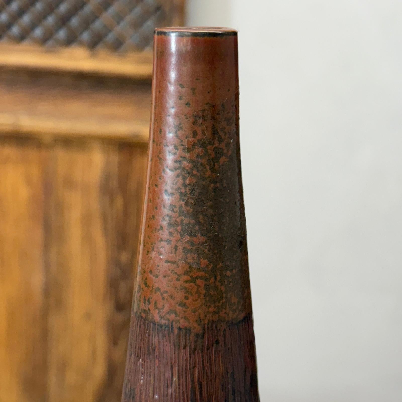 Close-up of a brown and copper textured ceramic vase in front of a wooden background.