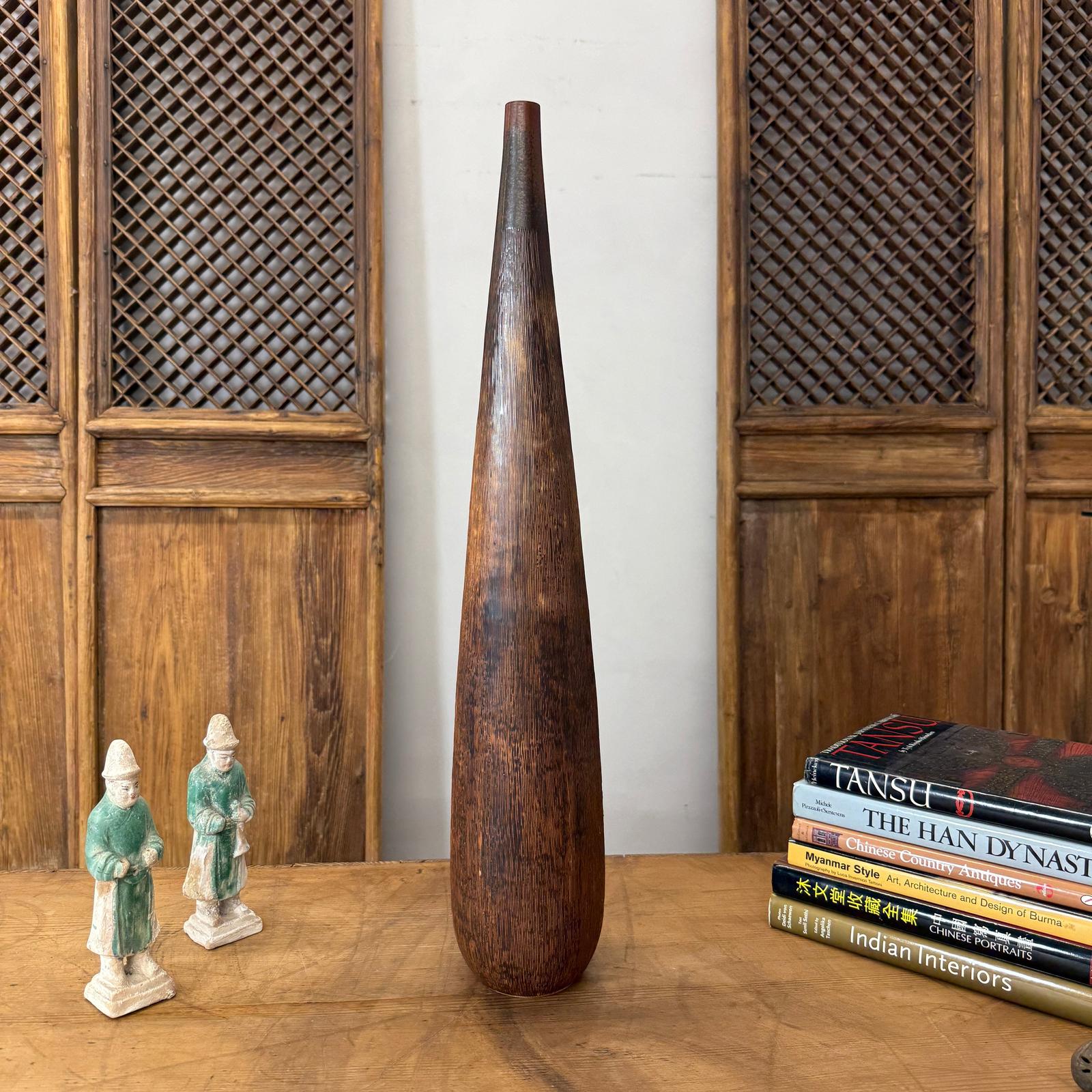 Brown and copper textured ceramic vase on table between two figurines, near books and wood panels.