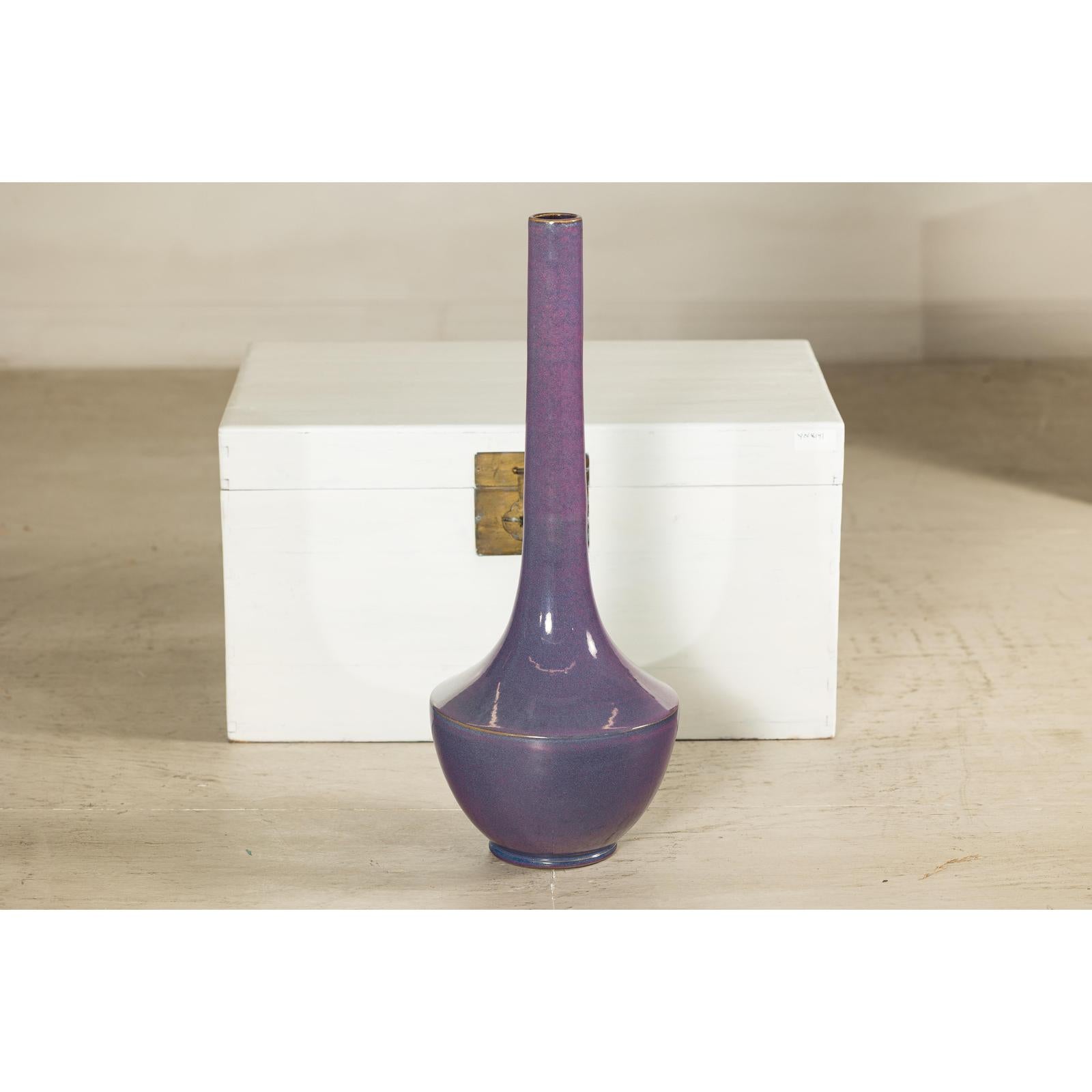 Purple ceramic vase with slender neck, artisan style, in front of a white wooden chest with brass latch.