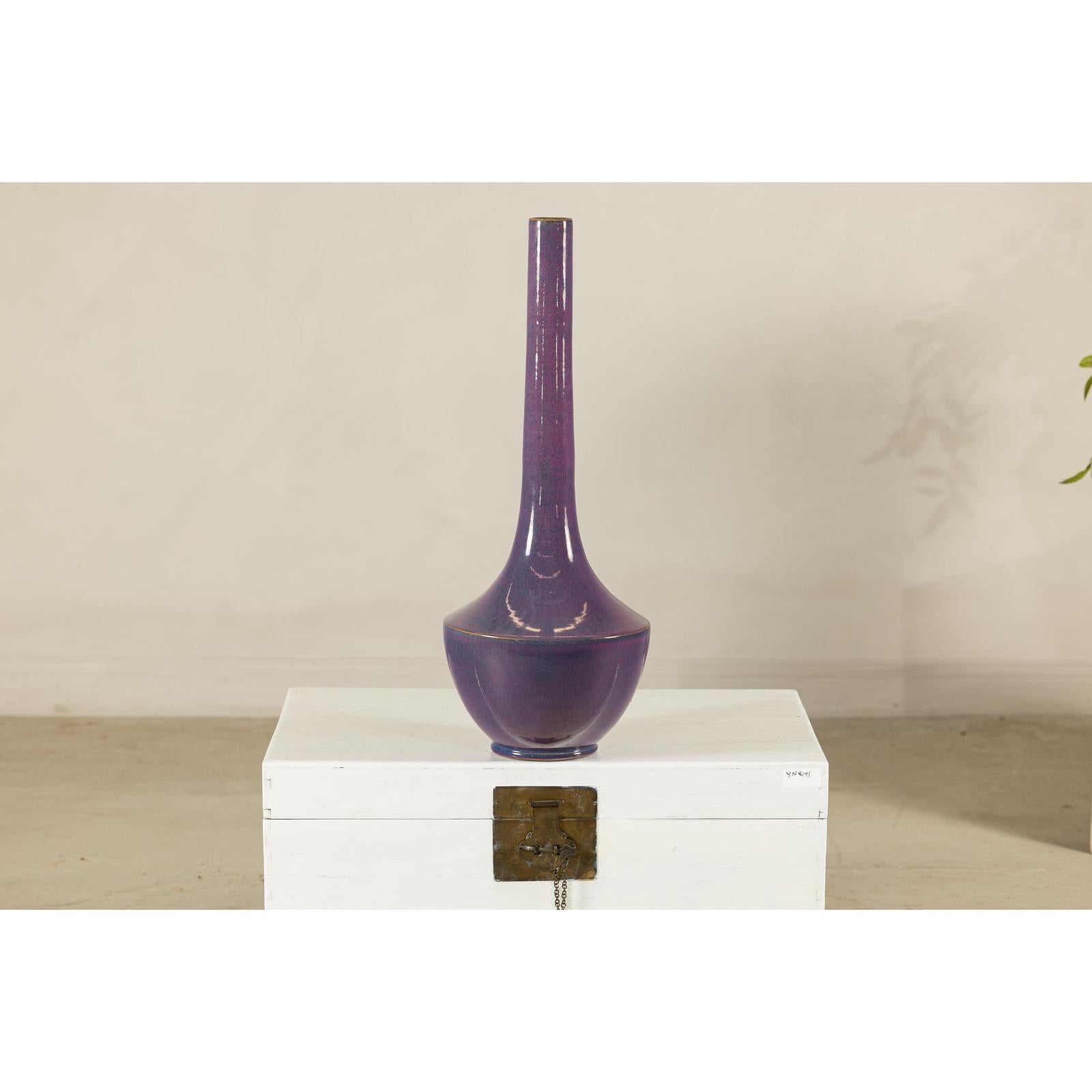 Purple ceramic vase with slender neck on white chest with metal clasp, close-up.