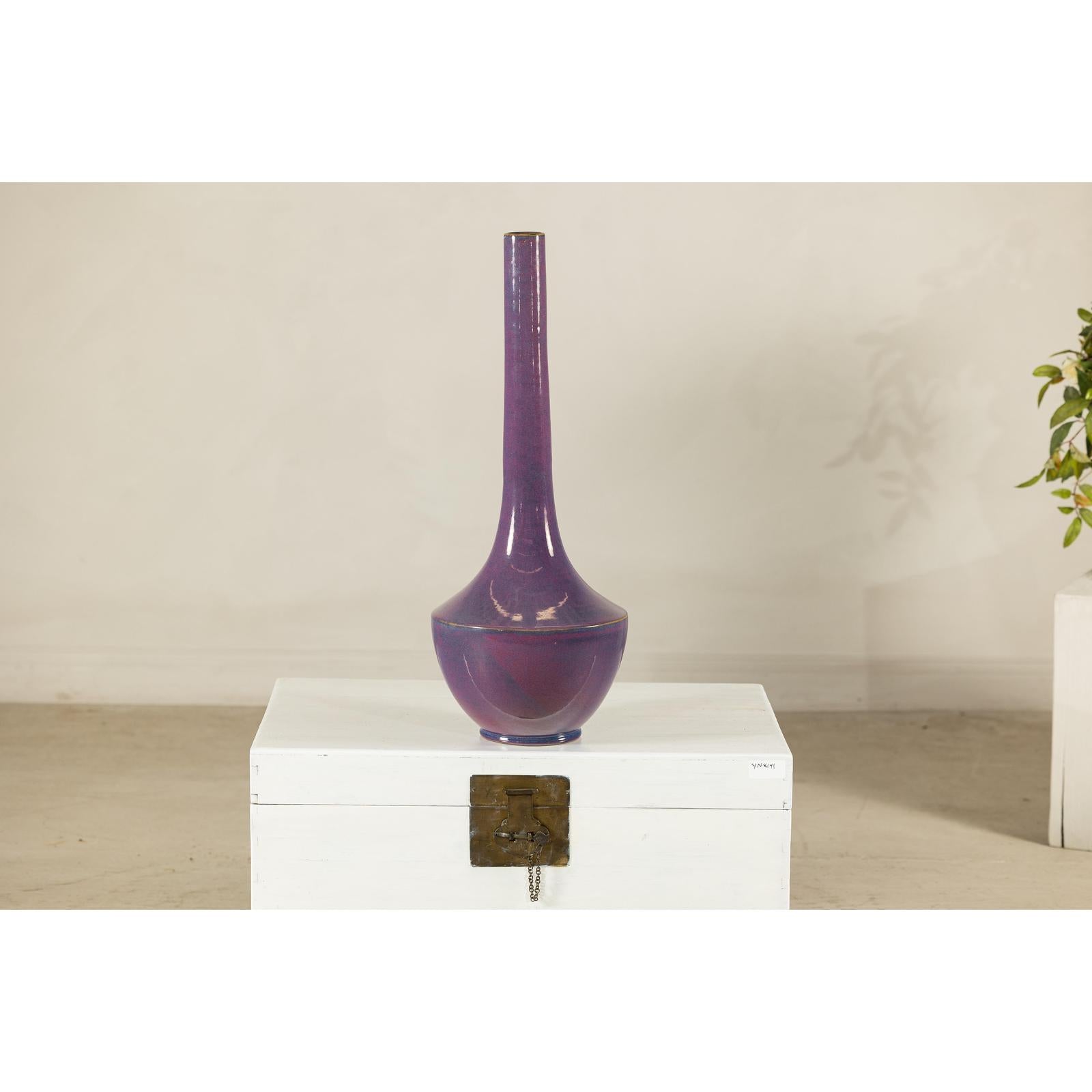 Purple glazed ceramic vase with slender neck on a white chest, light background, close-up.