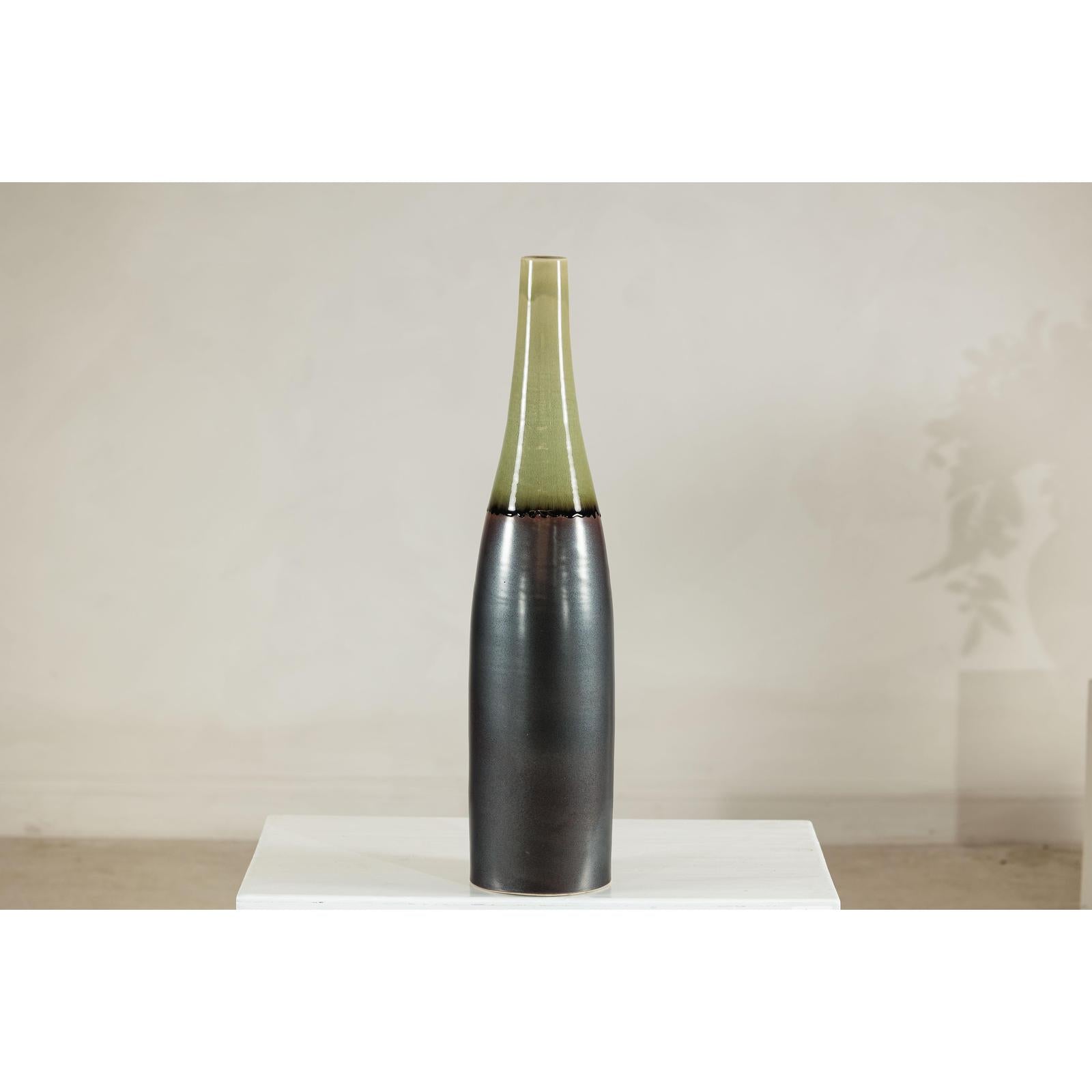 Charcoal ceramic vase with moss green glazed neck on white pedestal, light background, close-up view.