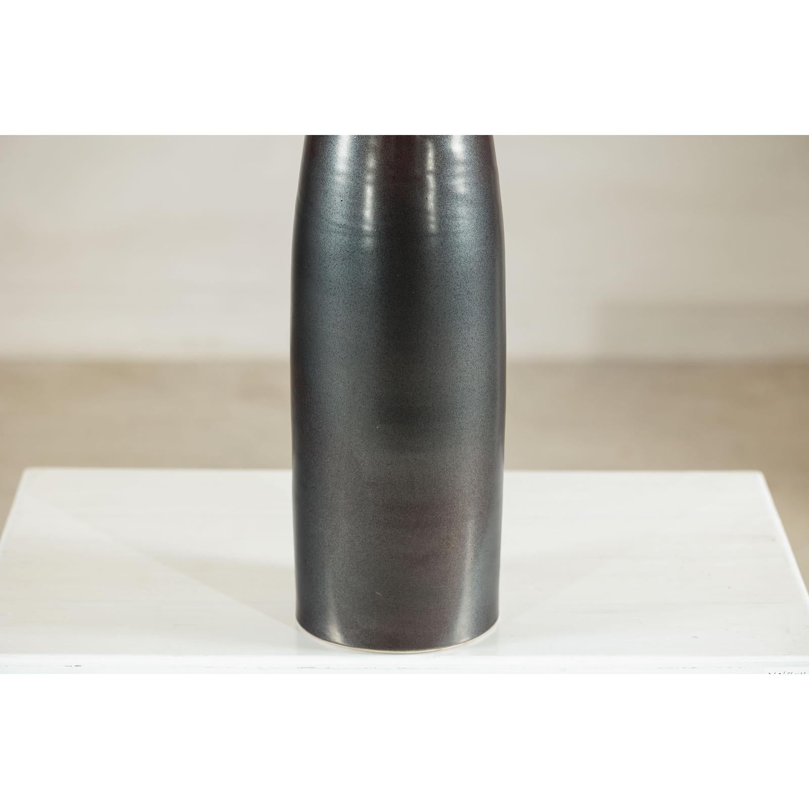 Charcoal ceramic vase with moss green glazed neck on a white surface, close-up.
