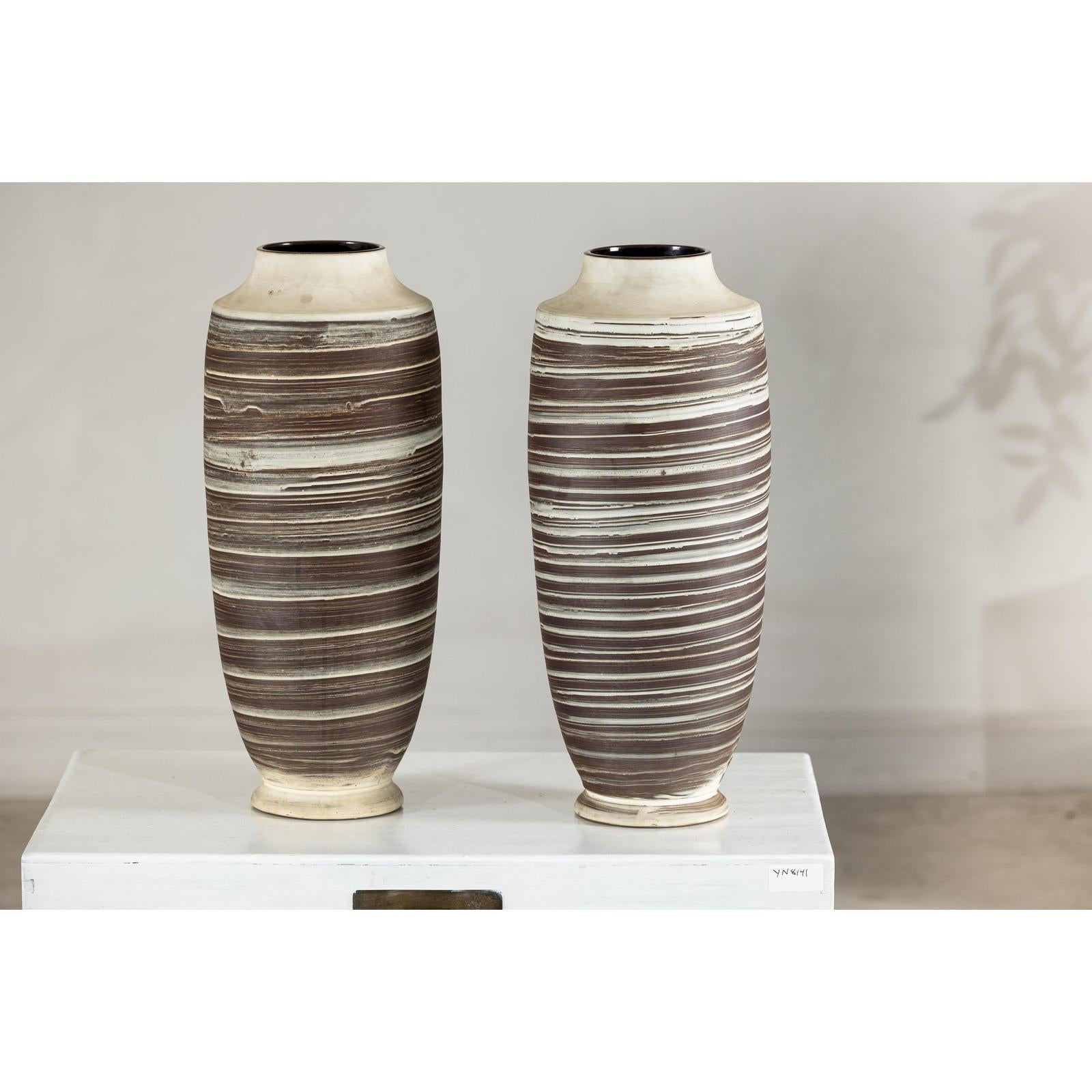 Close-up of two tall ceramic vases with horizontal swirl design on a white surface, neutral background.