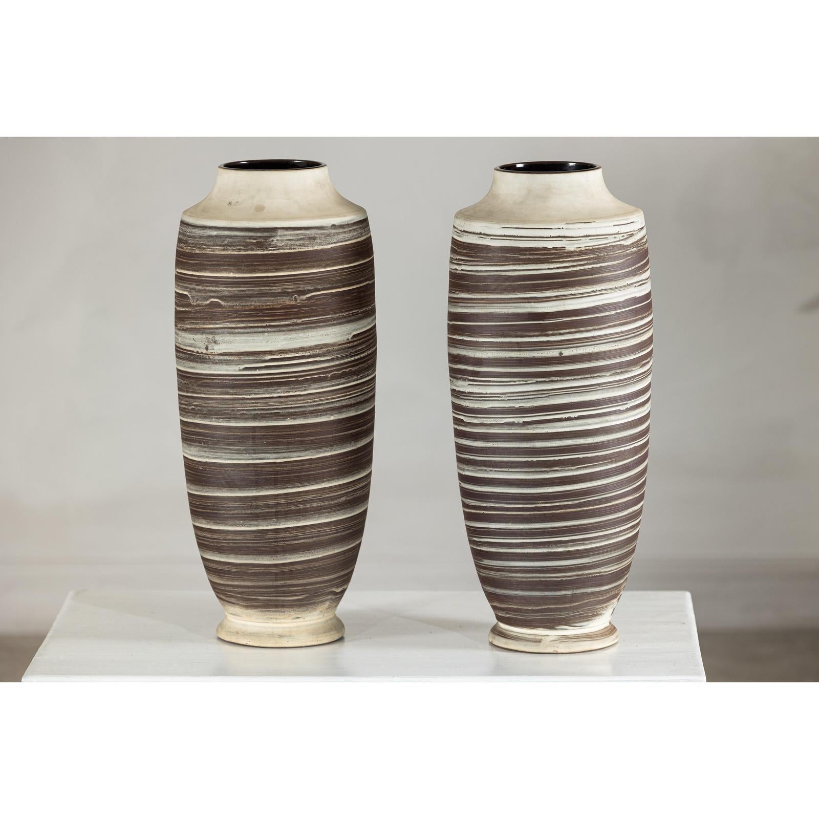 Close-up of two tall ceramic vases with horizontal swirl design, displayed on a white surface.