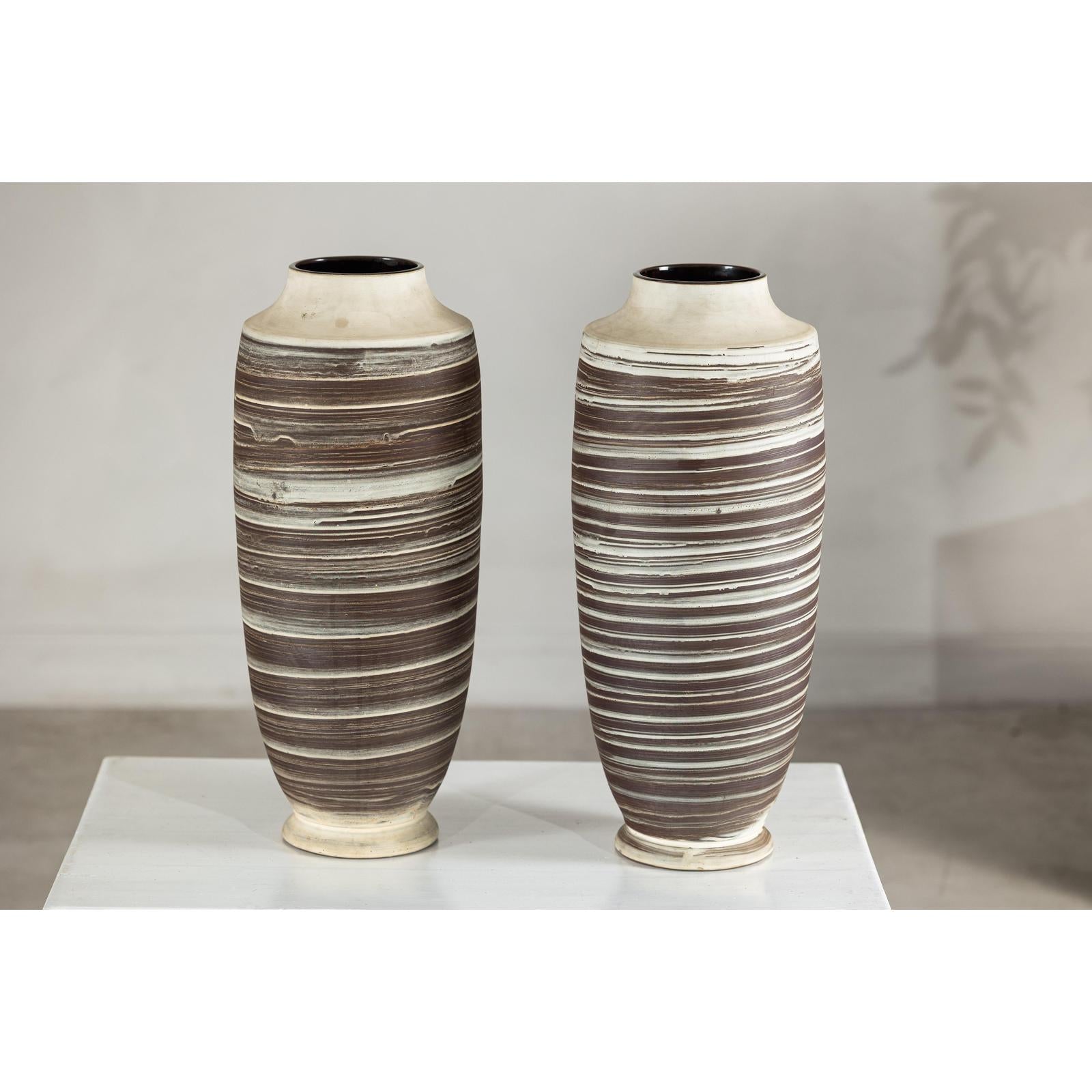 Close-up of two tall ceramic vases with horizontal swirl designs on a white surface against a neutral background.