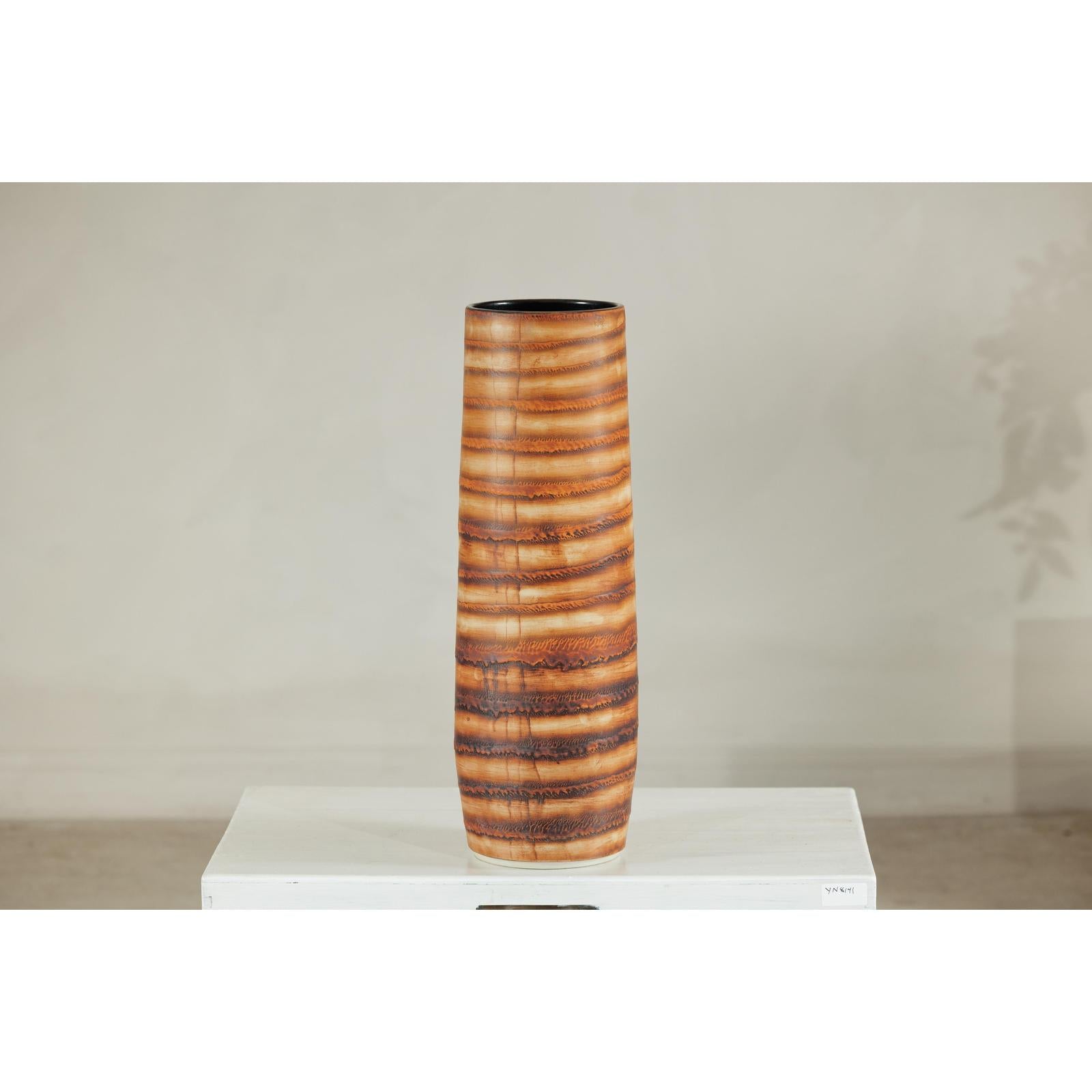 Orange-brown ceramic vase with swirl design, artisan style, on display against a neutral background.