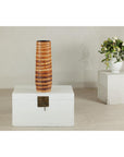 Orange-brown ceramic artisan vase with swirl design on white chest, white flower vase on pedestal in background.