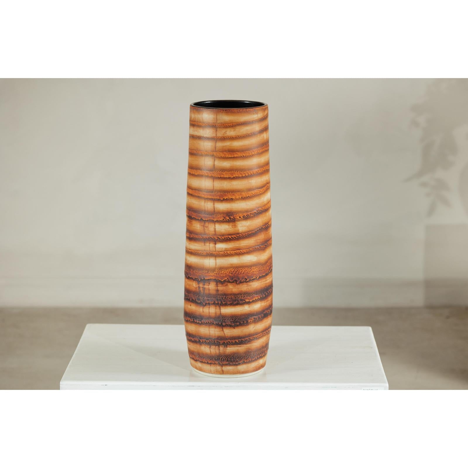 Orange-brown ceramic vase with swirl design, artisan style, on white pedestal against neutral background.