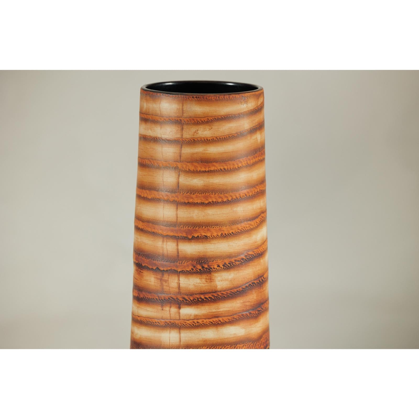 Close-up of tall orange-brown ceramic vase with swirling patterns, handcrafted in a sleek cylindrical shape.