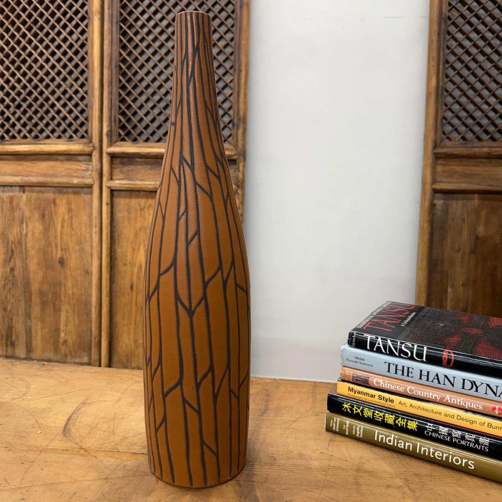 Sand brown and orange ceramic vase with black crackle design on a wooden table next to books and wood panels.
