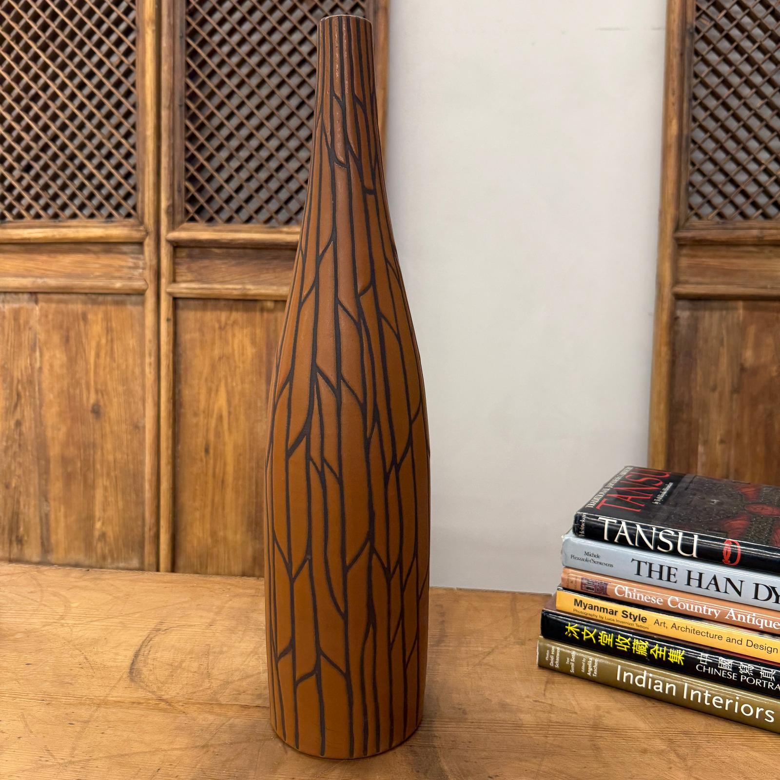 Sand brown orange ceramic vase with black crackle design beside stacked books on a wooden table.
