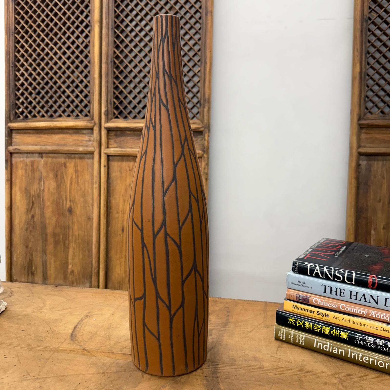 Sand brown and orange ceramic vase with black crackle design on wooden table next to a stack of books.