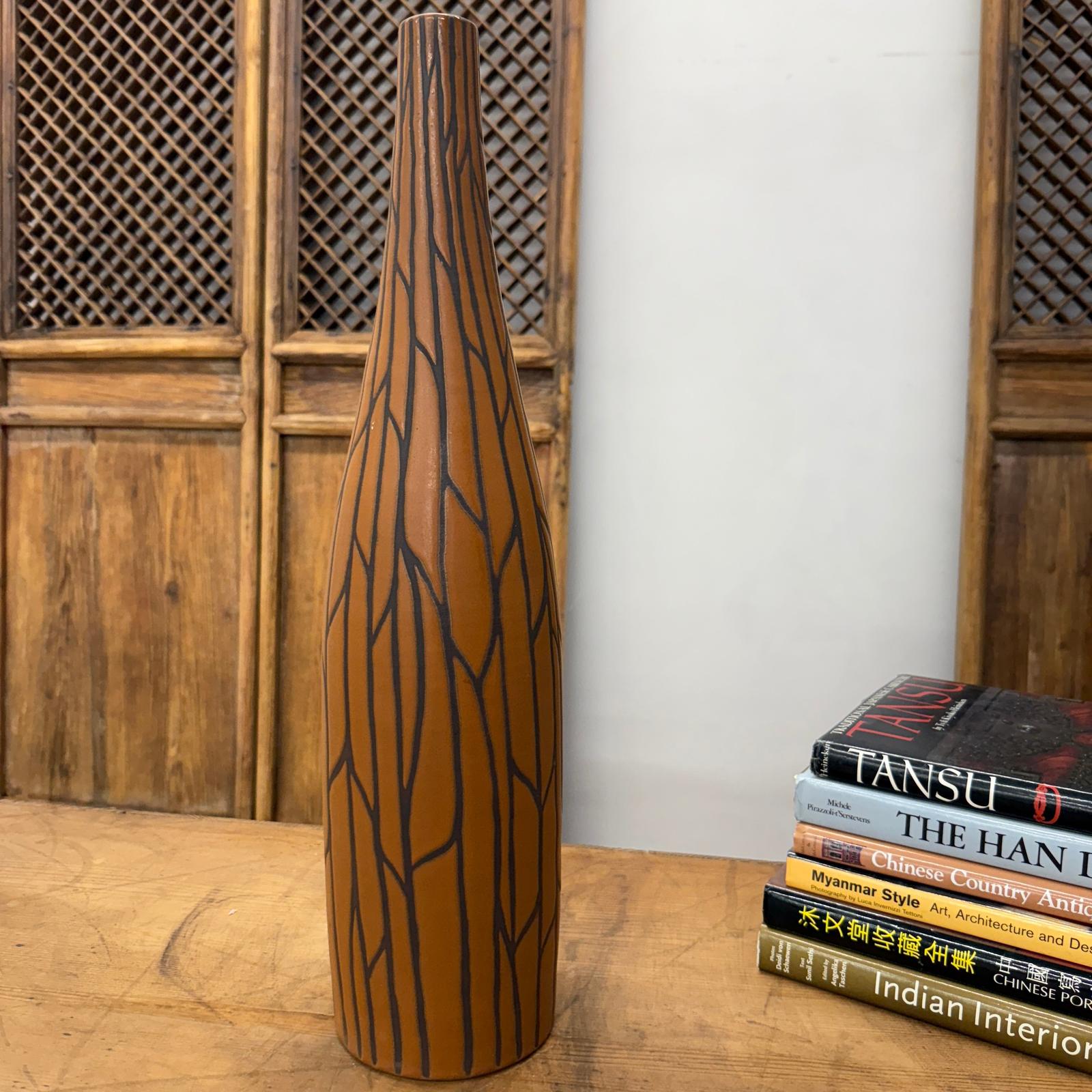 Sand brown and orange vase with black crackle design on wooden table next to a stack of books.