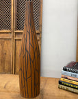 Sand brown and orange vase with black crackle design on wooden table next to a stack of books.