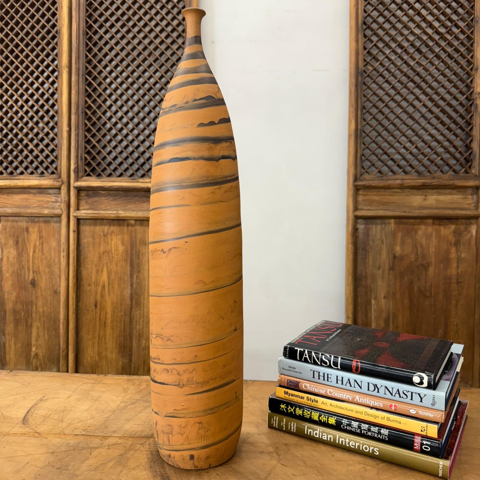 Orange ceramic vase with black swirl on wooden table next to stacked antique and design books.