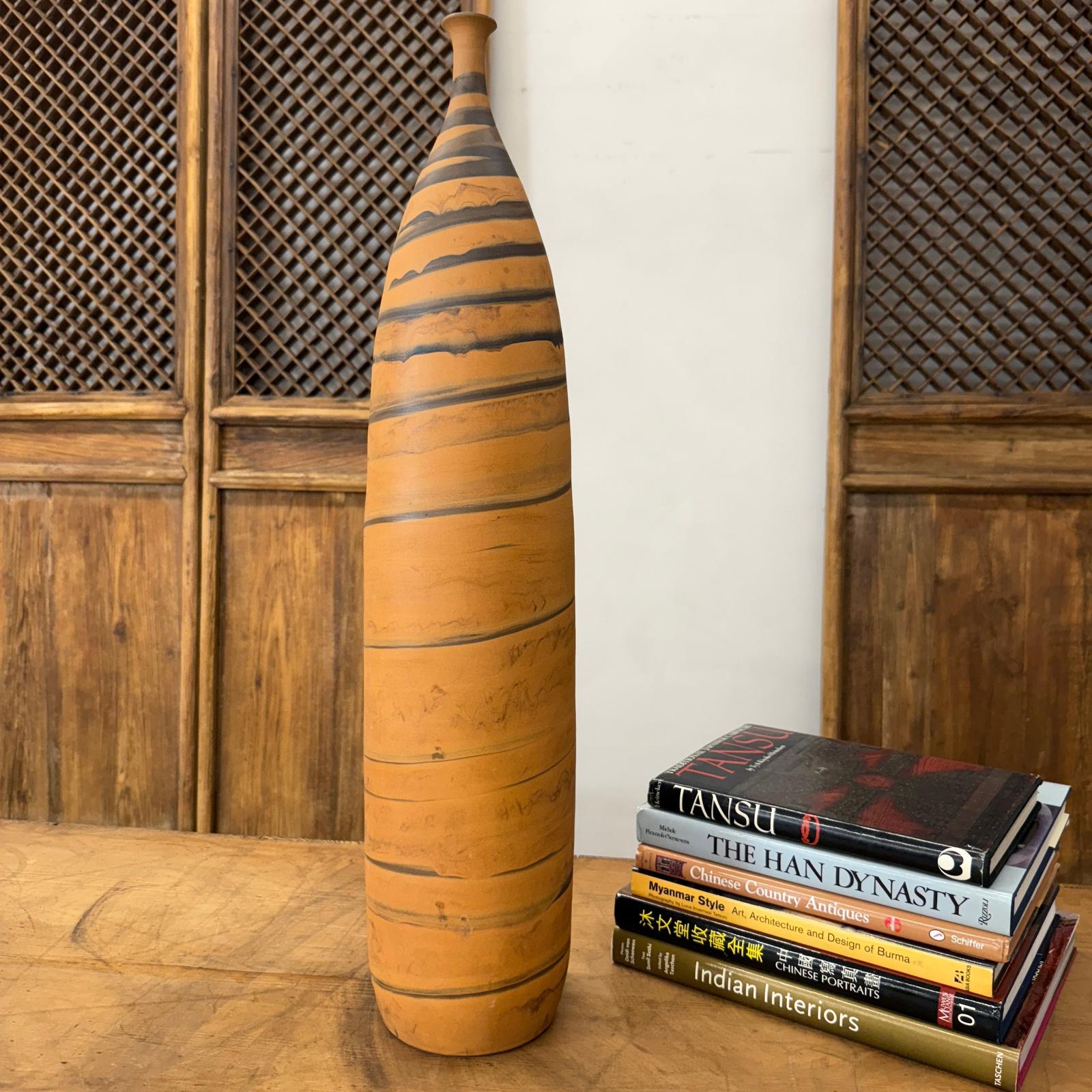 Orange ceramic vase with black swirl next to books on a wood table with carved wood backdrop.