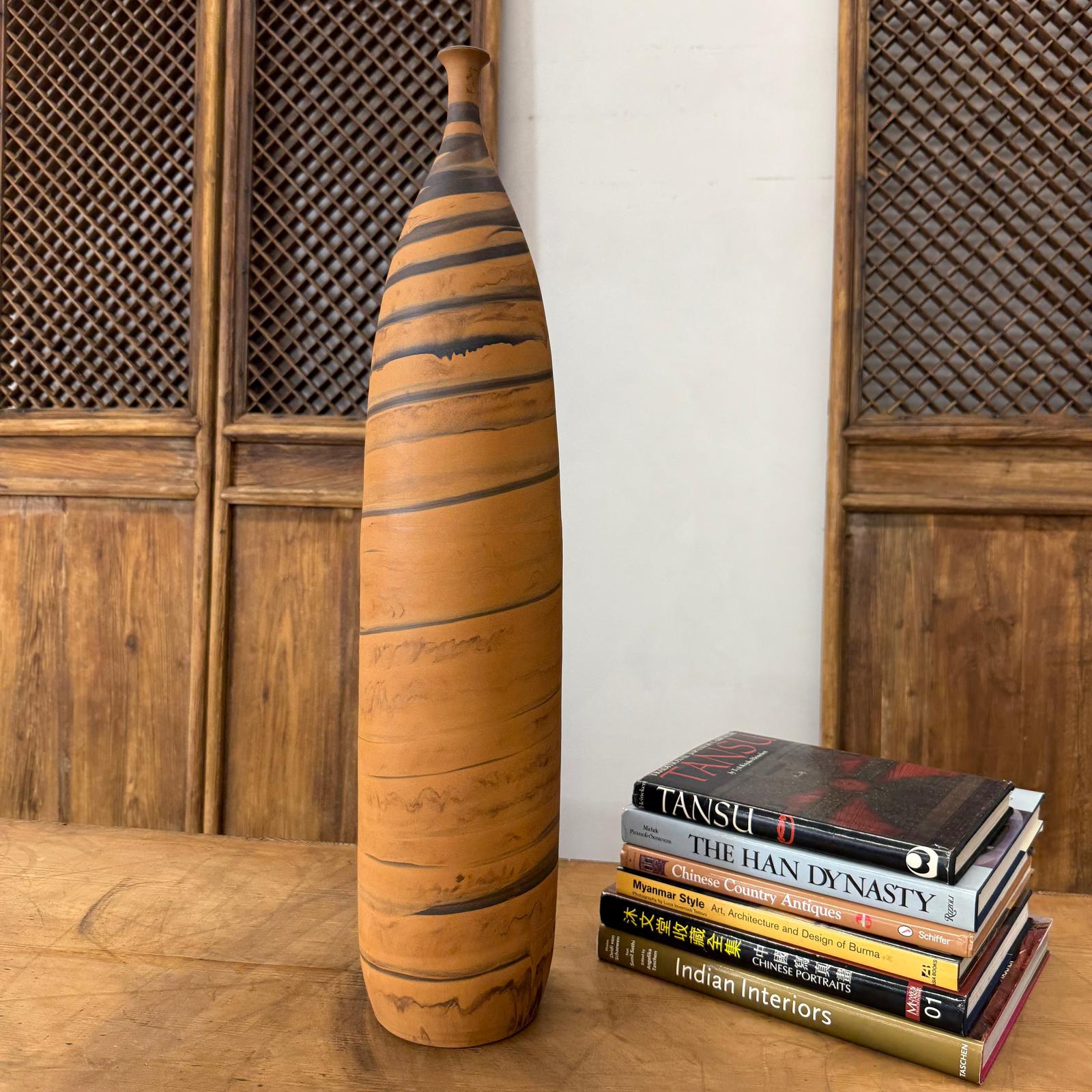 Orange and black ceramic vase with swirl design on wooden table beside books, wood panel background.