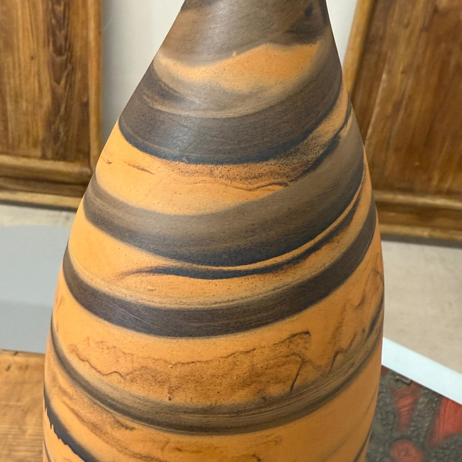 Close-up of orange vase with black swirl, tall and skinny, ceramic, on wooden background.