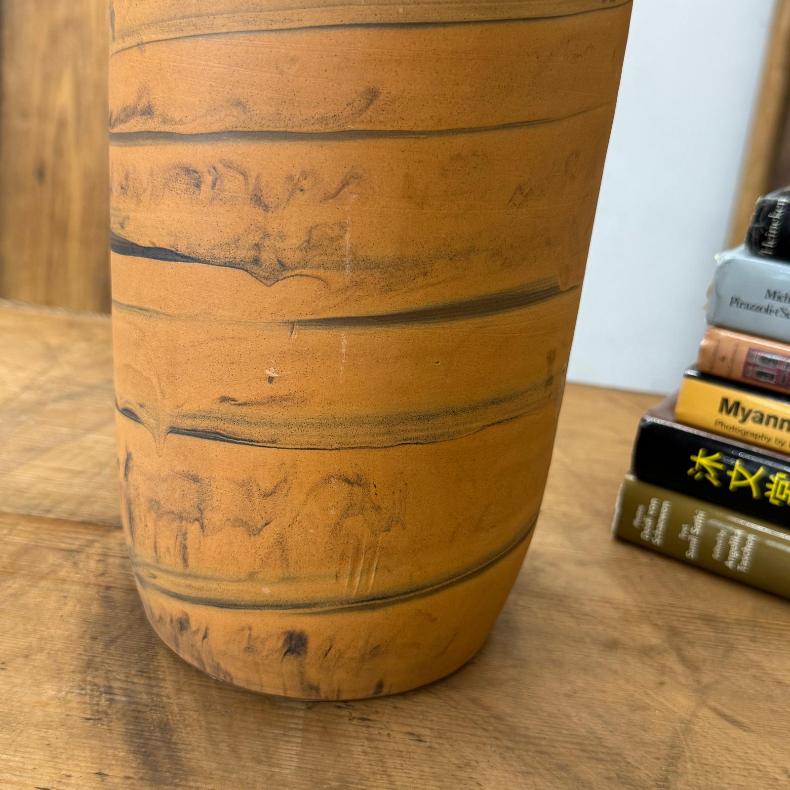 Close-up of an orange vase with black swirl, ceramic, beside stacked books on a wooden surface.