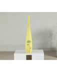 Yellow ceramic vase with hand-painted flowers, tall and skinny, on white pedestal against a plain wall.