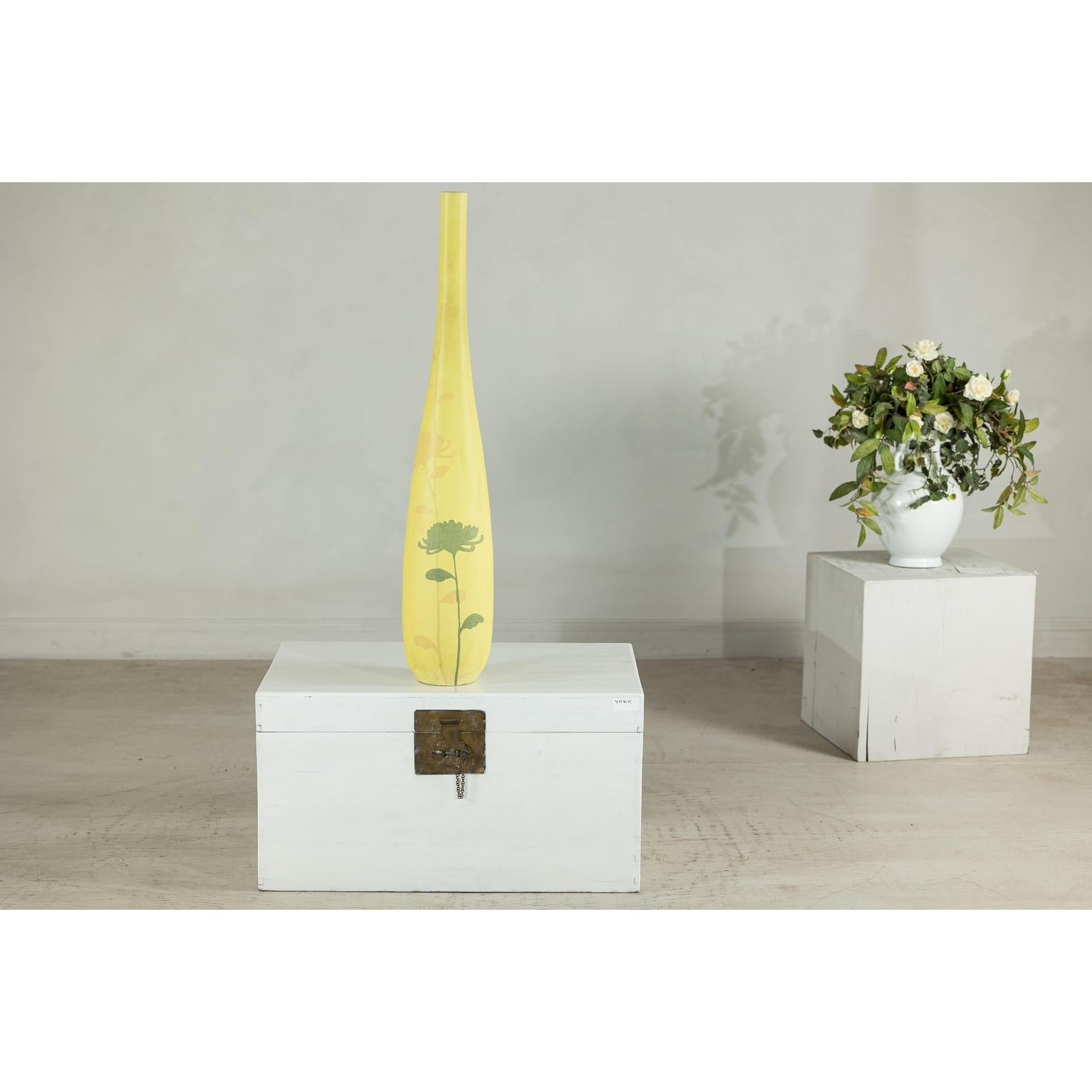 Yellow ceramic vase with hand-painted flowers on white chest, next to white vase with flowers, indoor setting.
