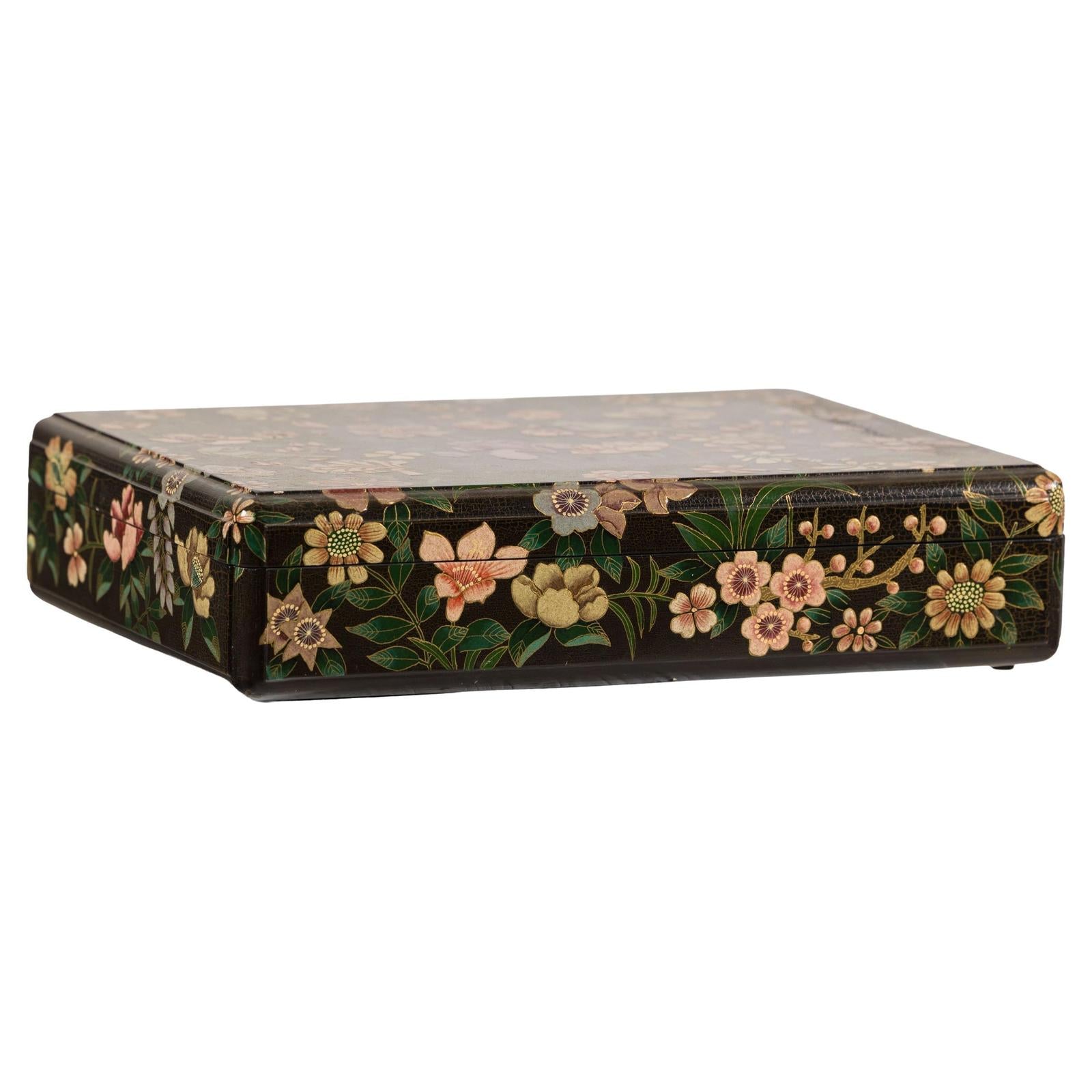 Close-up of black lacquer box with colorful painted flowers and birds, felt interior visible, on dark background.