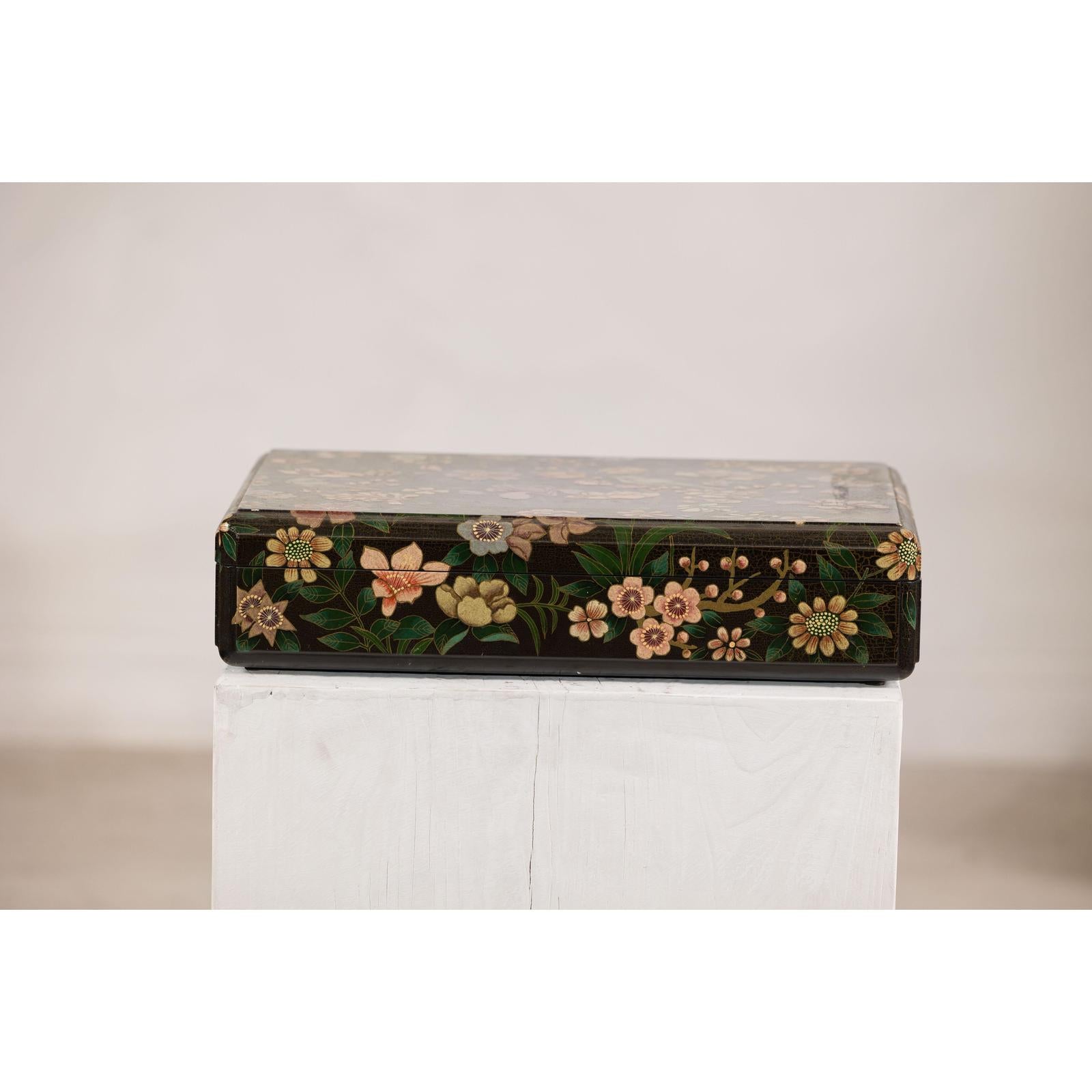 Black lacquer box with floral and bird designs, felt interior, displayed on a white pedestal against a plain background.