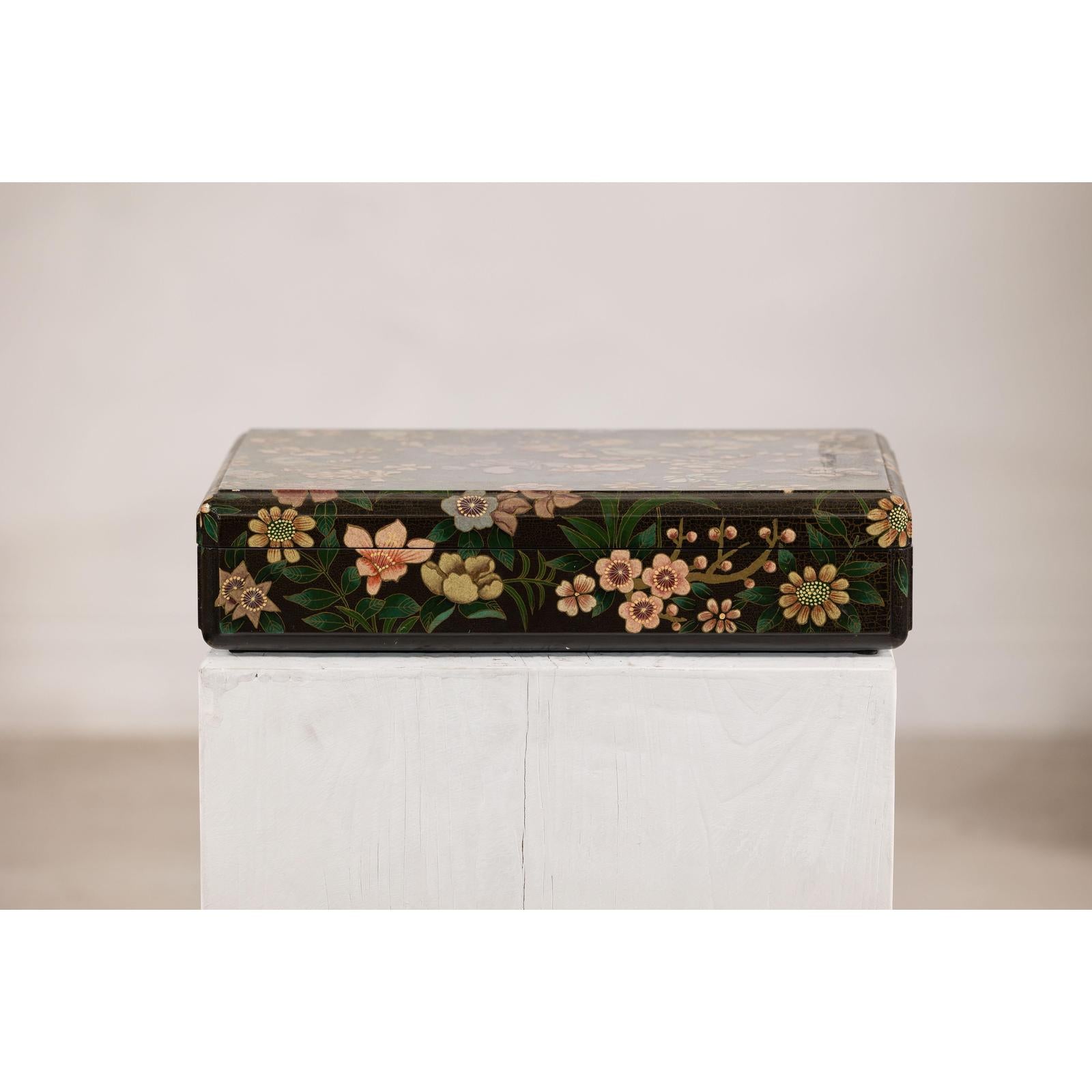 Black lacquer box with painted flowers and birds, felt interior, displayed on a white pedestal against plain background.