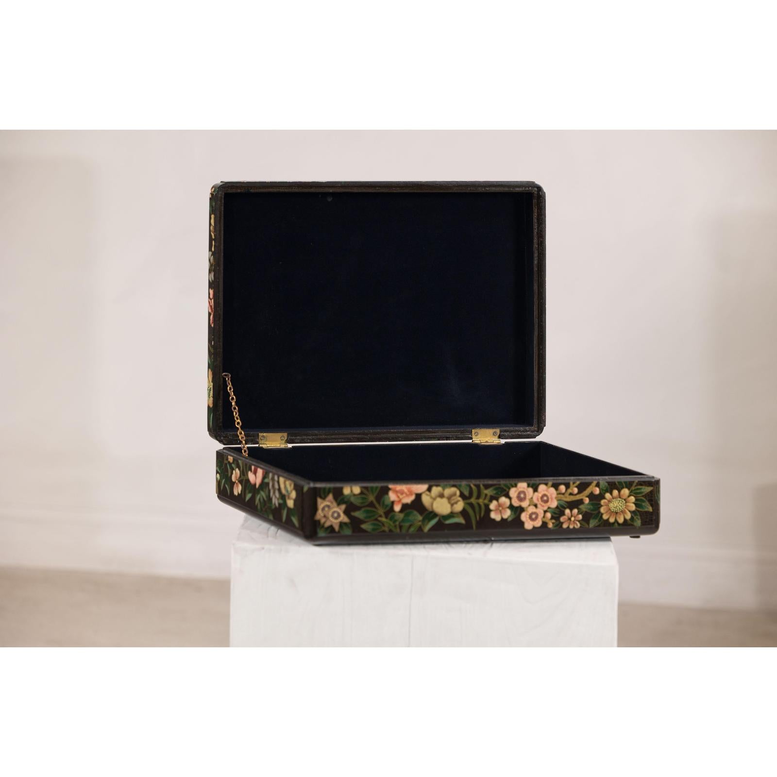 Close-up of a black lacquer box with floral and bird design, felt interior, open on a white pedestal.