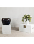 Close-up of a vintage brown and blue glazed ceramic planter with rounded form on a white pedestal next to flowers.