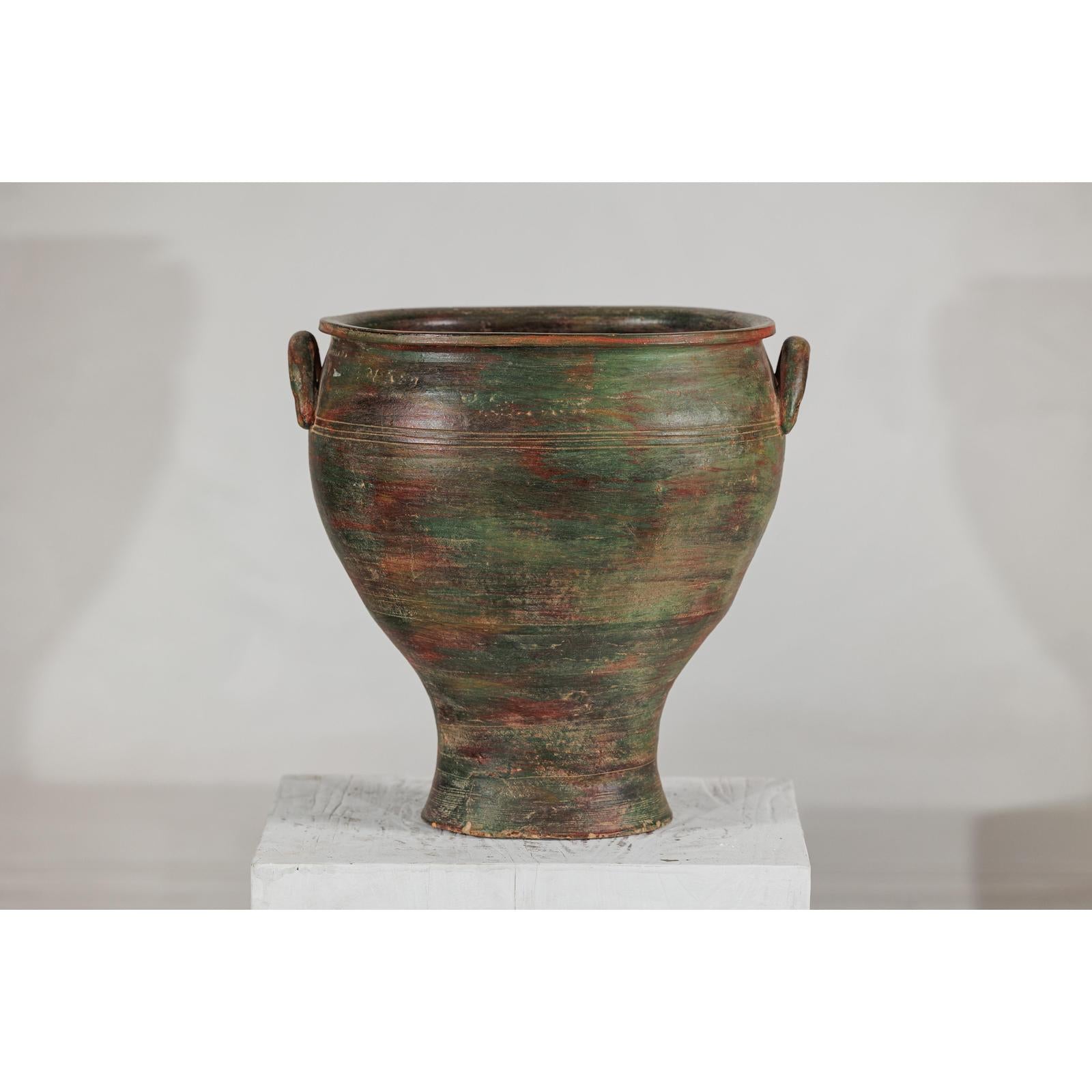 Close-up of a green, brown, and red vintage ceramic planter on a white pedestal against a plain background.