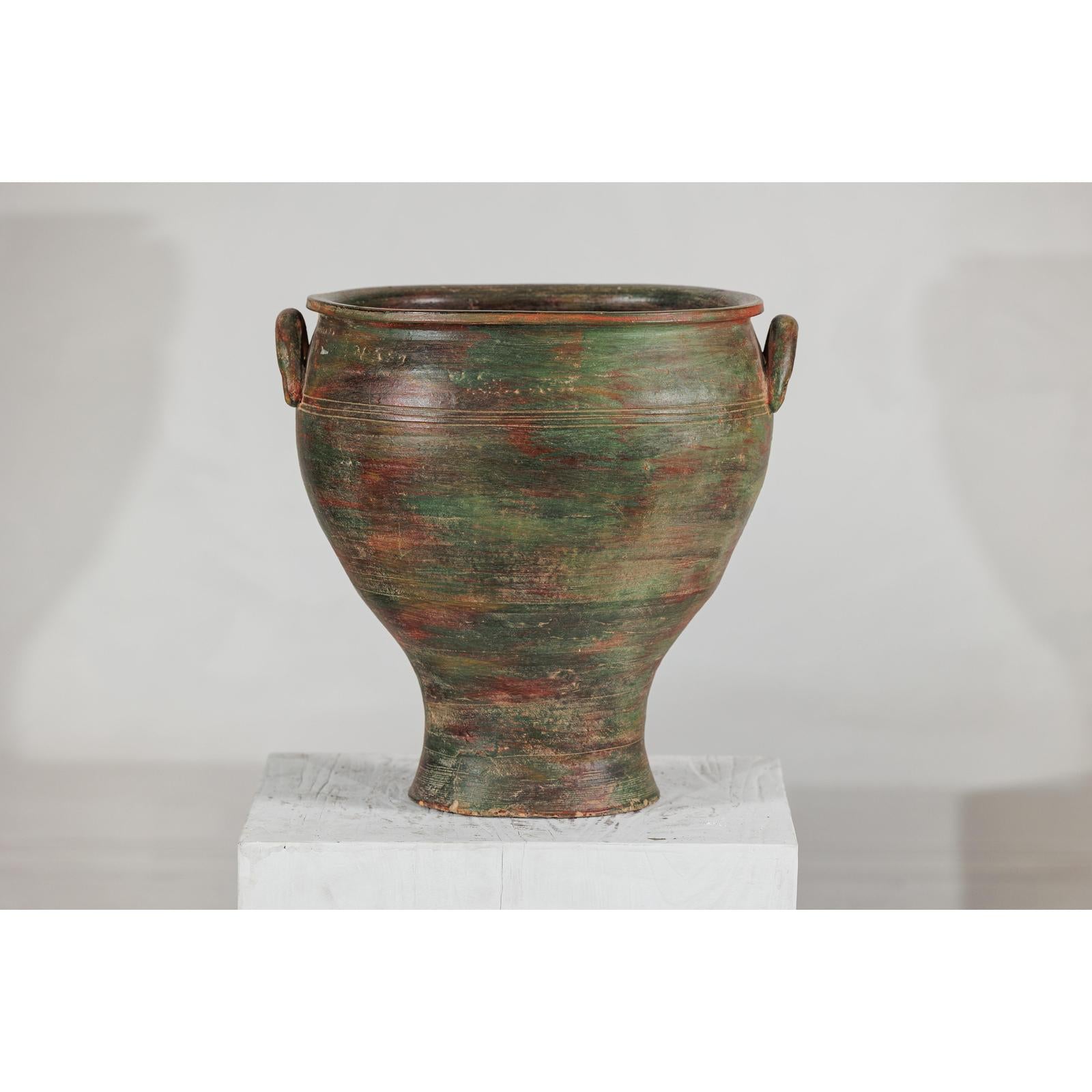 Green, brown, and red ceramic planter in vintage style on a white pedestal against a plain background.