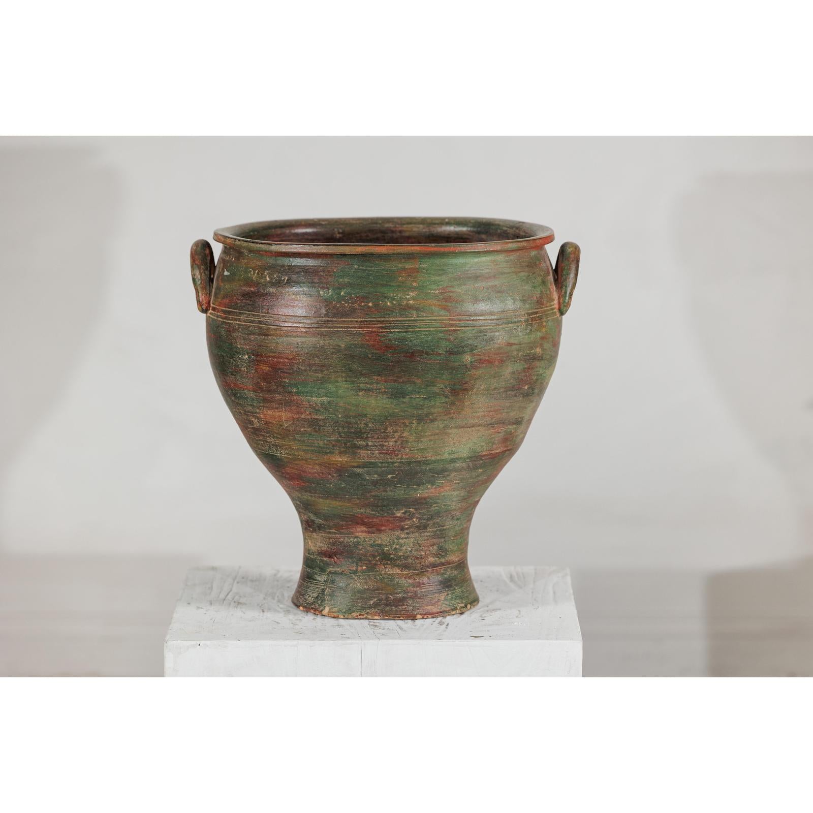 Green, brown, and red vintage ceramic planter with side handles on a white pedestal, close-up view.