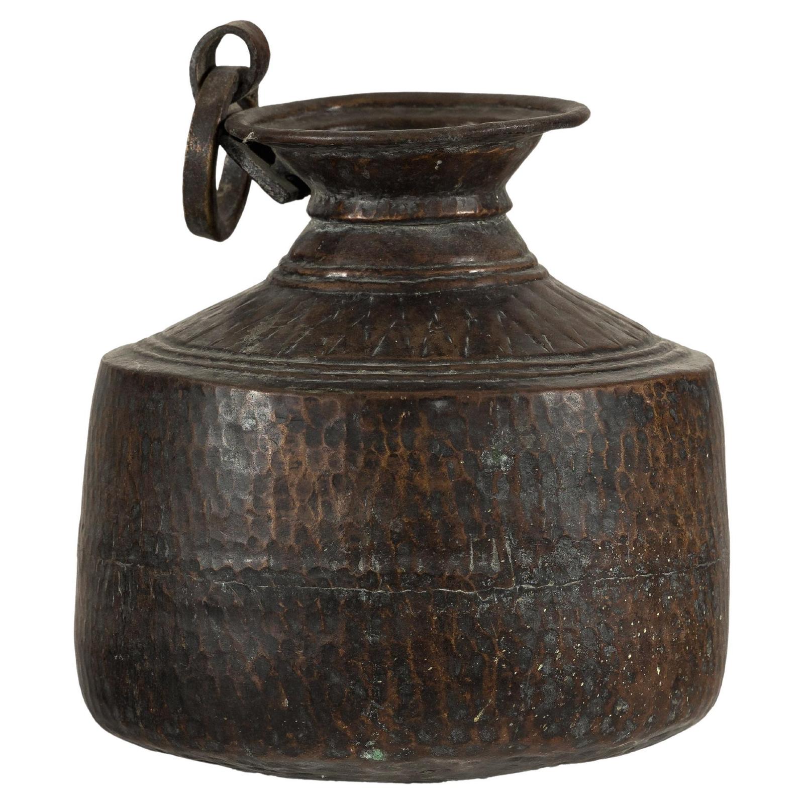 Copper hand-hammered vintage metal jug with round body and ring handle, close-up on plain background.