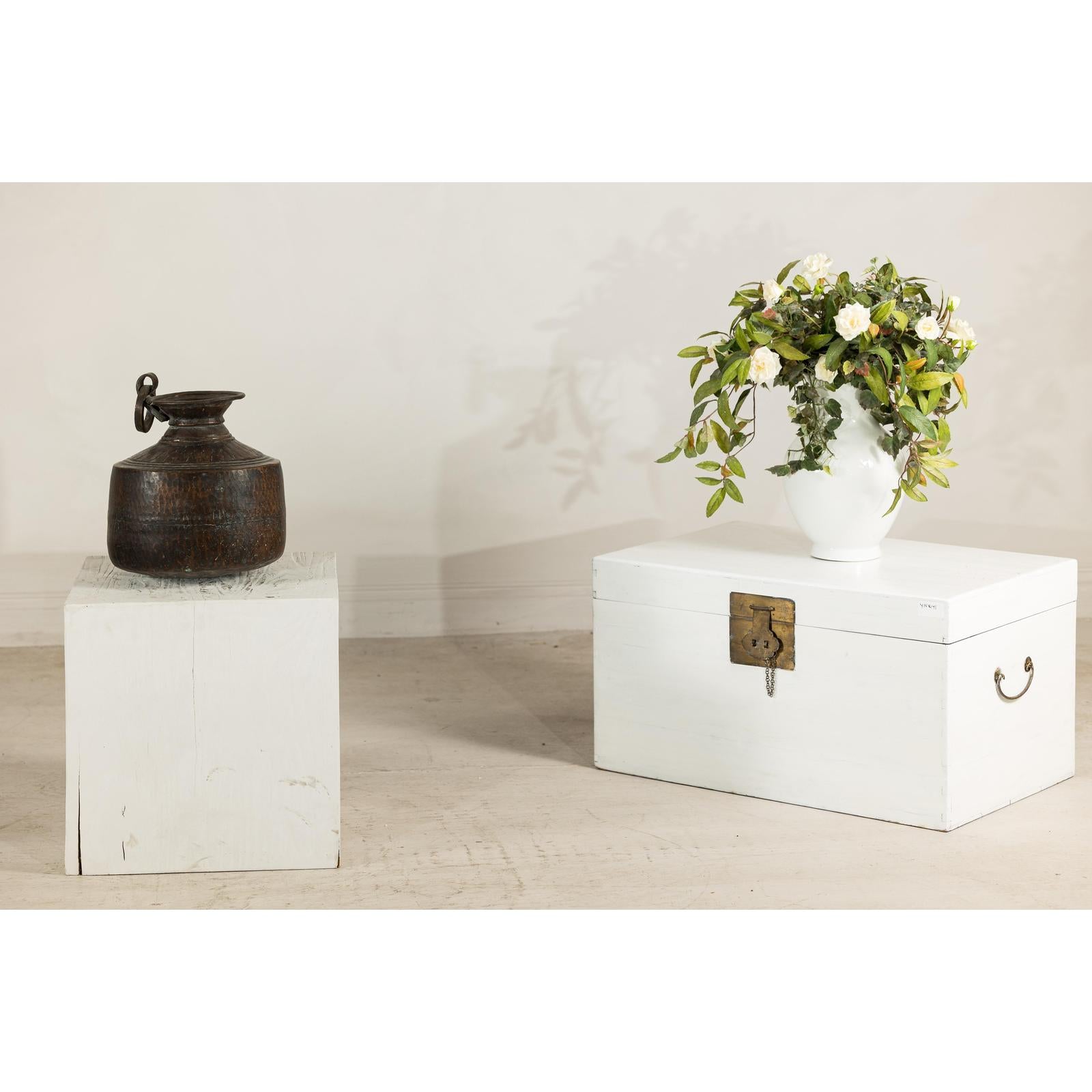 Silver metal hand-hammered jug with ring handle on white cube, minimal decor and plain background.